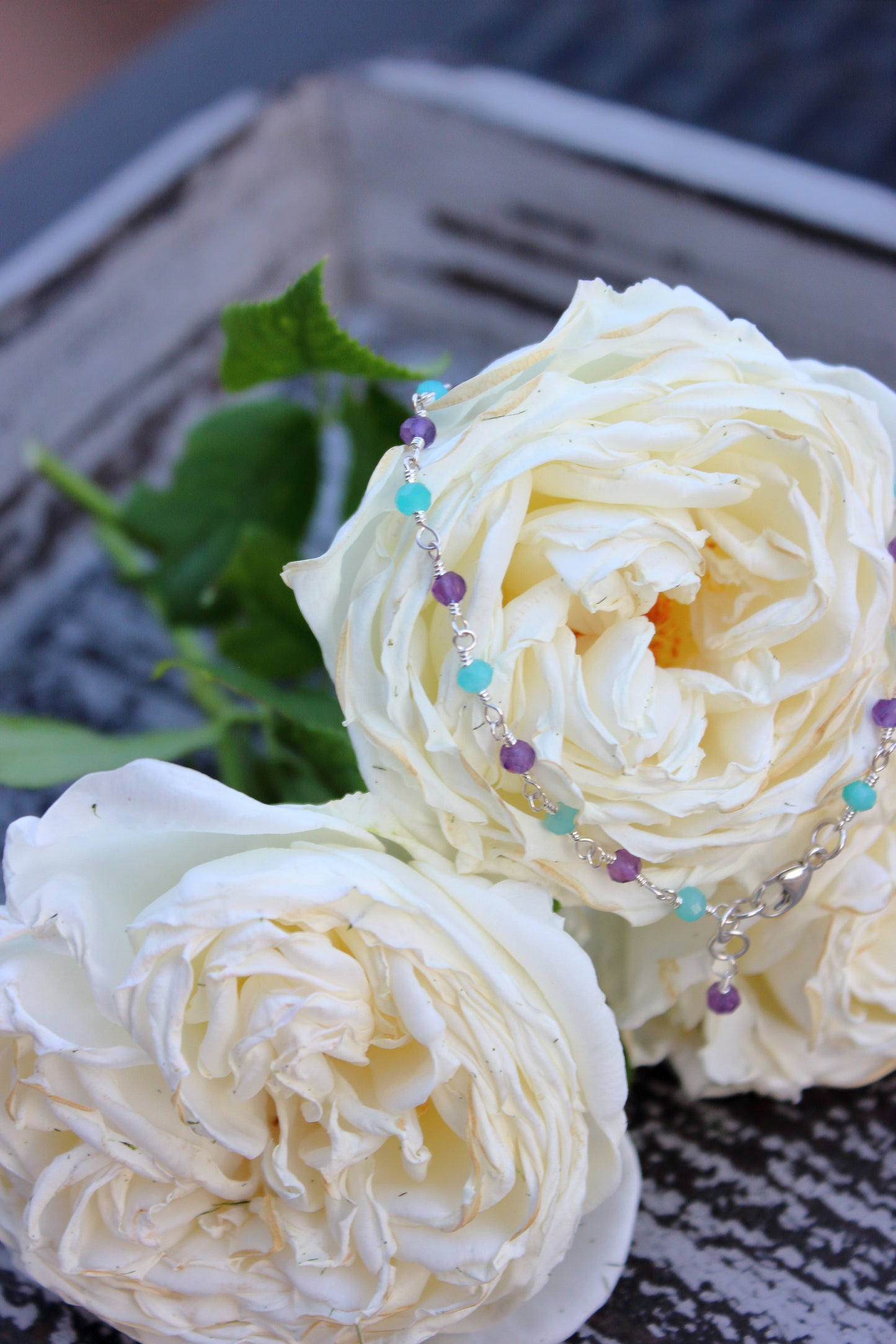 Two white roses with a beaded bracelet on a textured surface