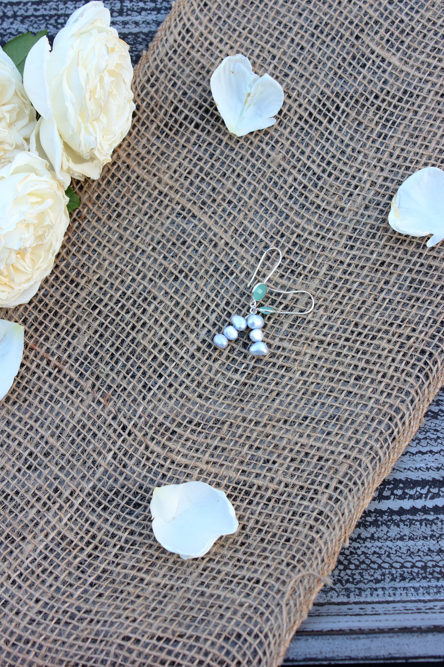 Silver earrings with small stones on a burlap surface with white flowers.