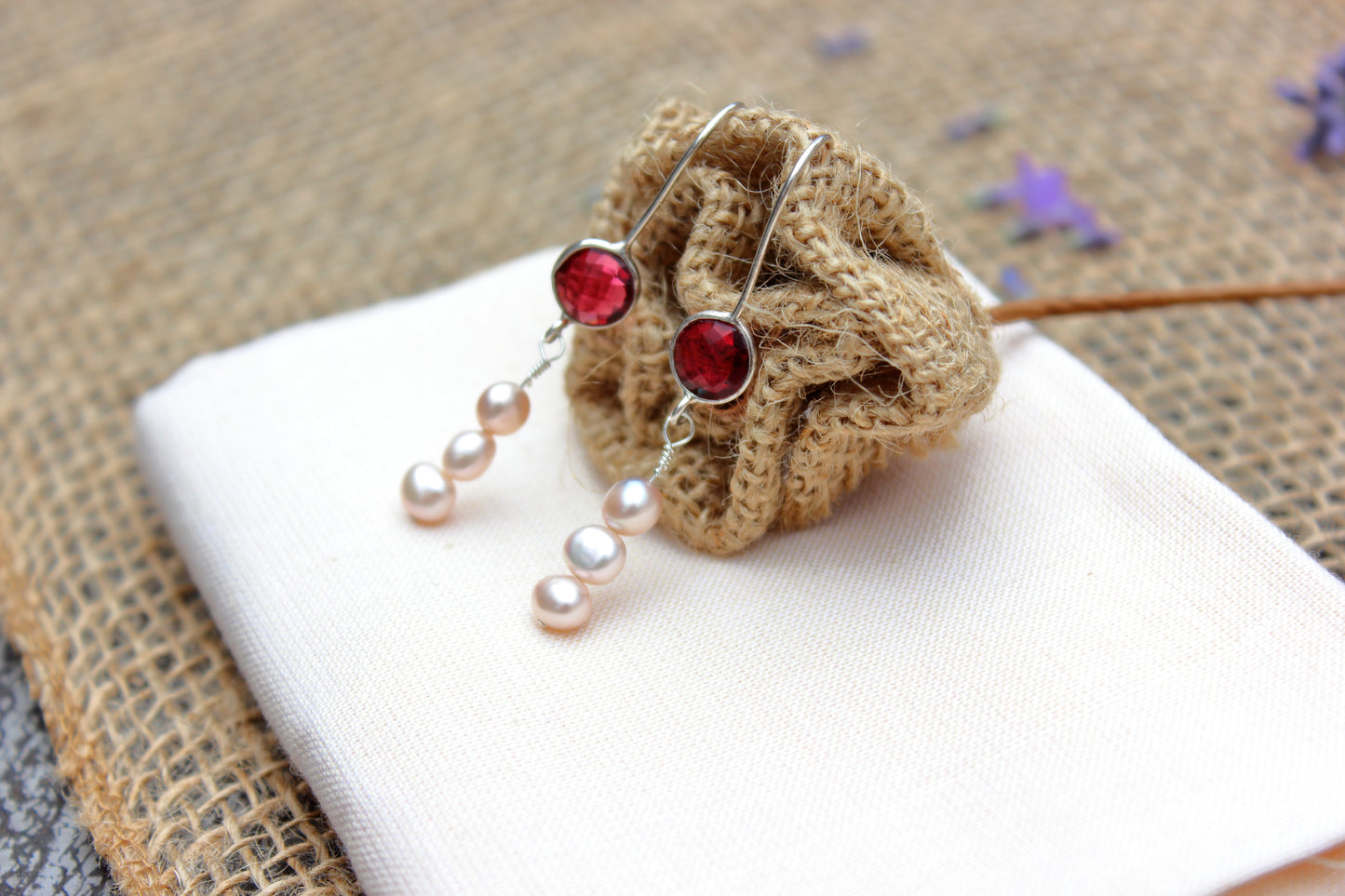 Pair of earrings with pink gemstones and pearl-like beads on a textured surface