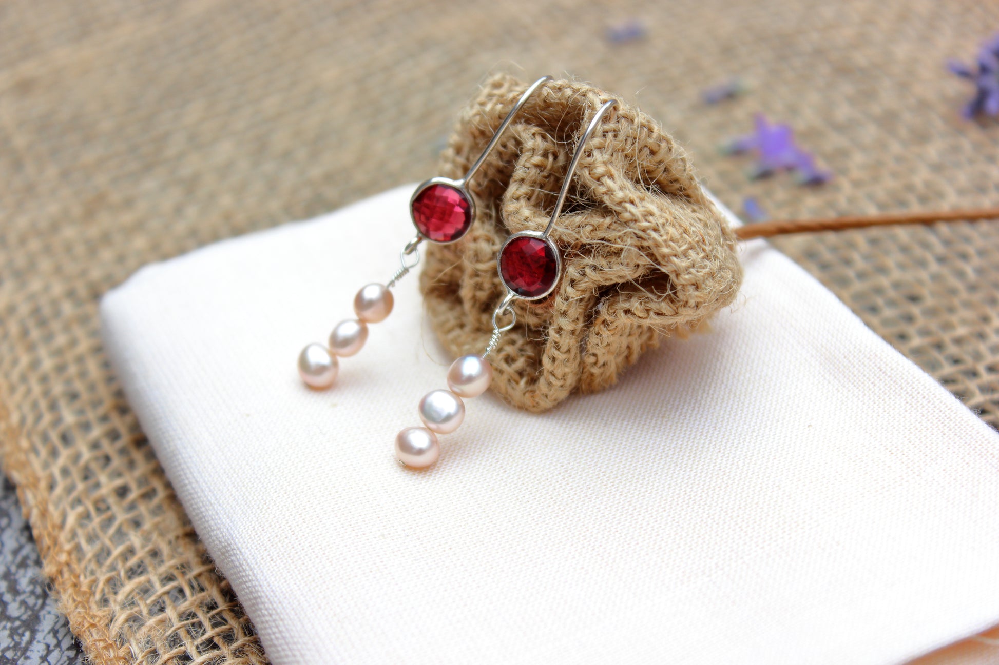 Pair of earrings with pink gemstones and pearl-like beads on a textured surface