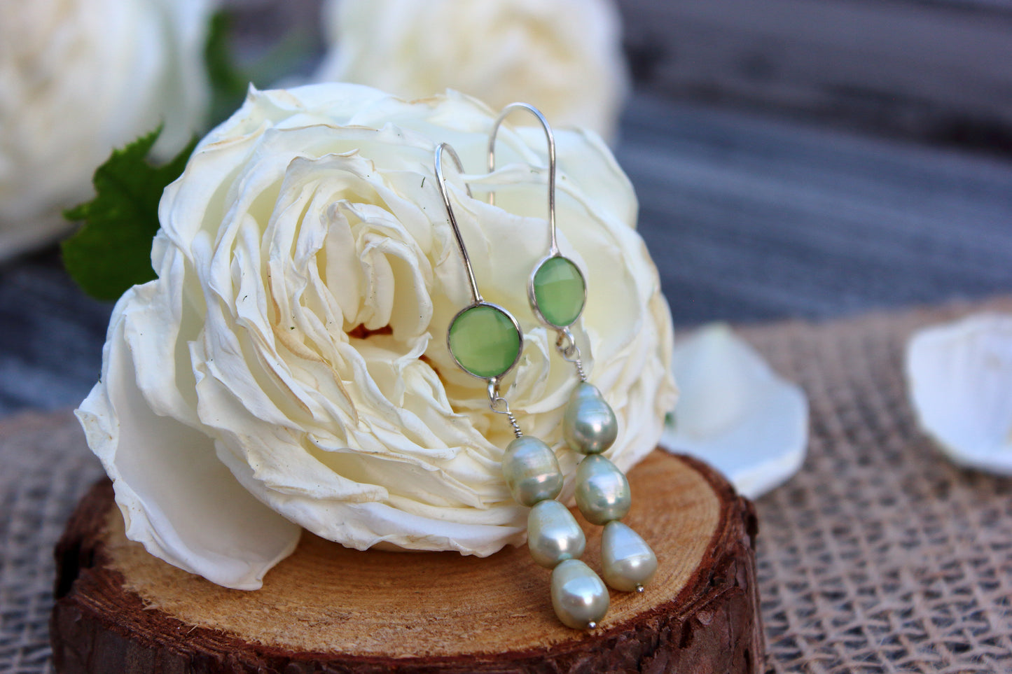 Green earrings with pearls on a white rose on a wooden block