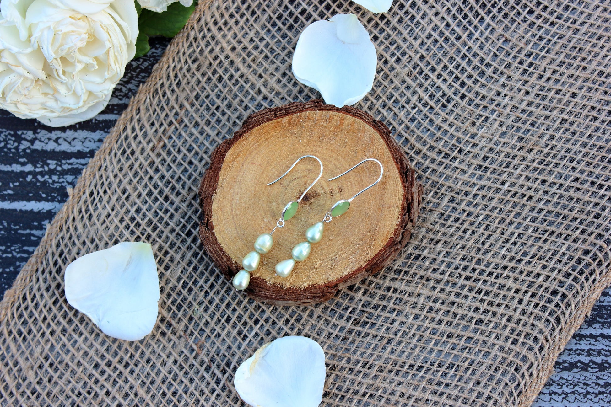 Pearl earrings on a wooden slice with white flowers on a textured surface