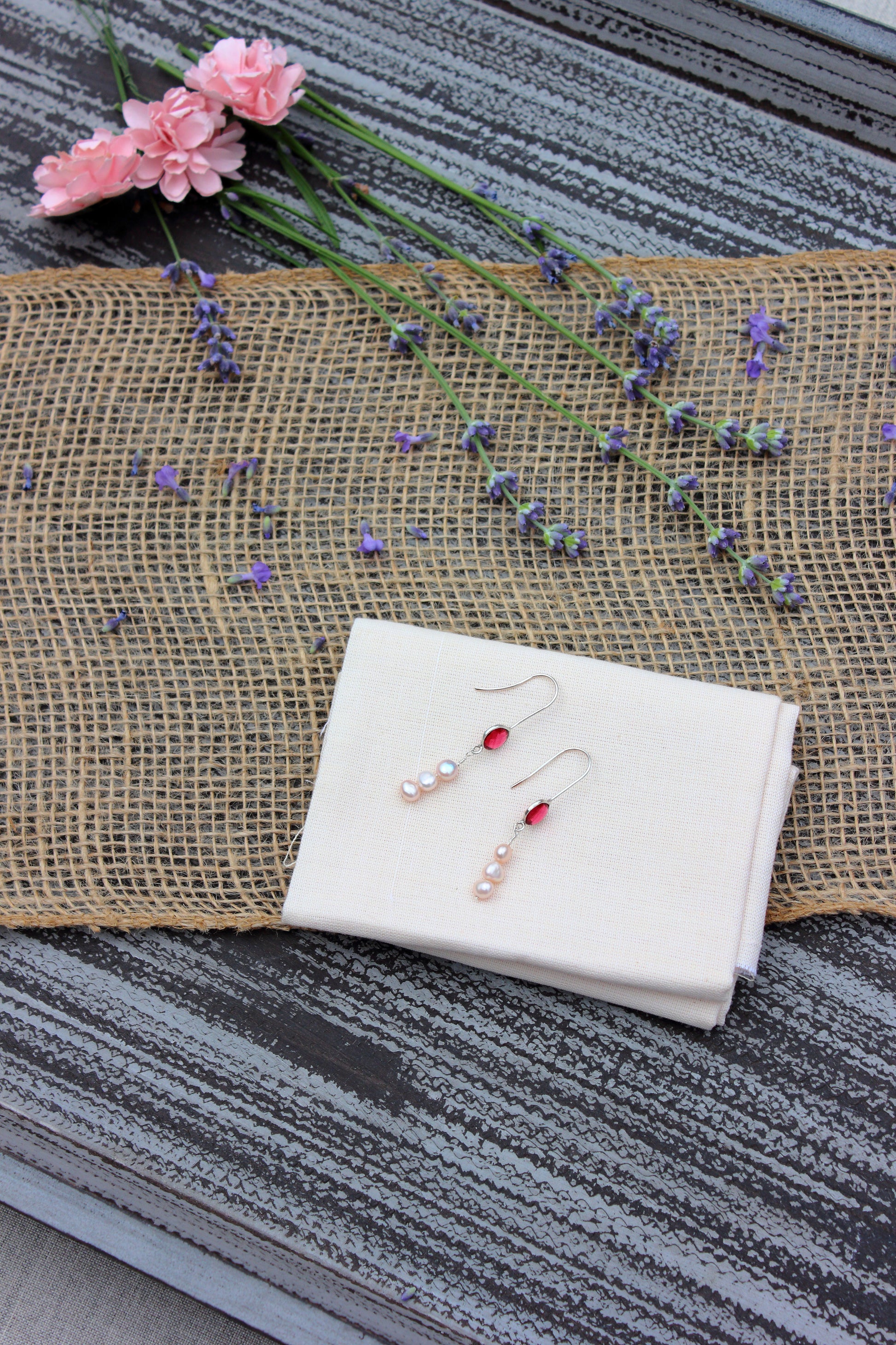 Pair of earrings on a white cloth with flowers in the background