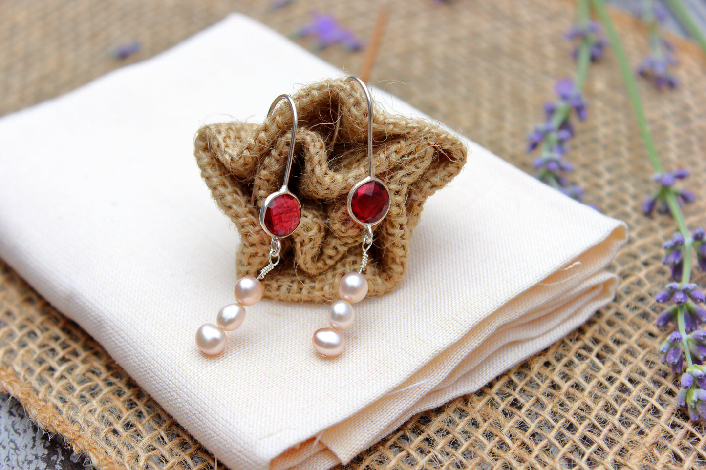 Pair of earrings with pink stones and pearl-like elements on a white cloth with a textured background.