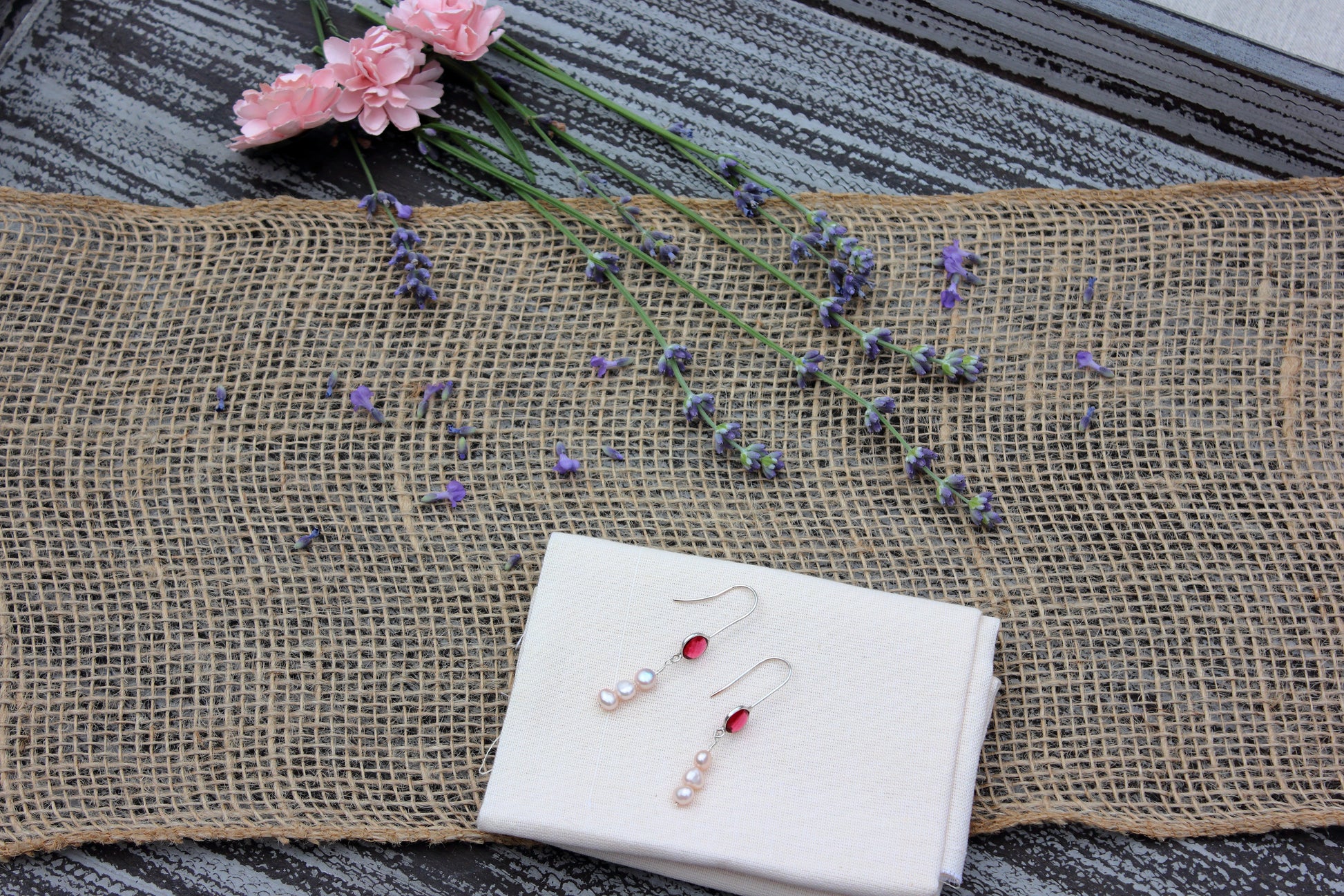 Pearl and pink earrings on a white cloth with lavender and pink flowers on a textured surface.