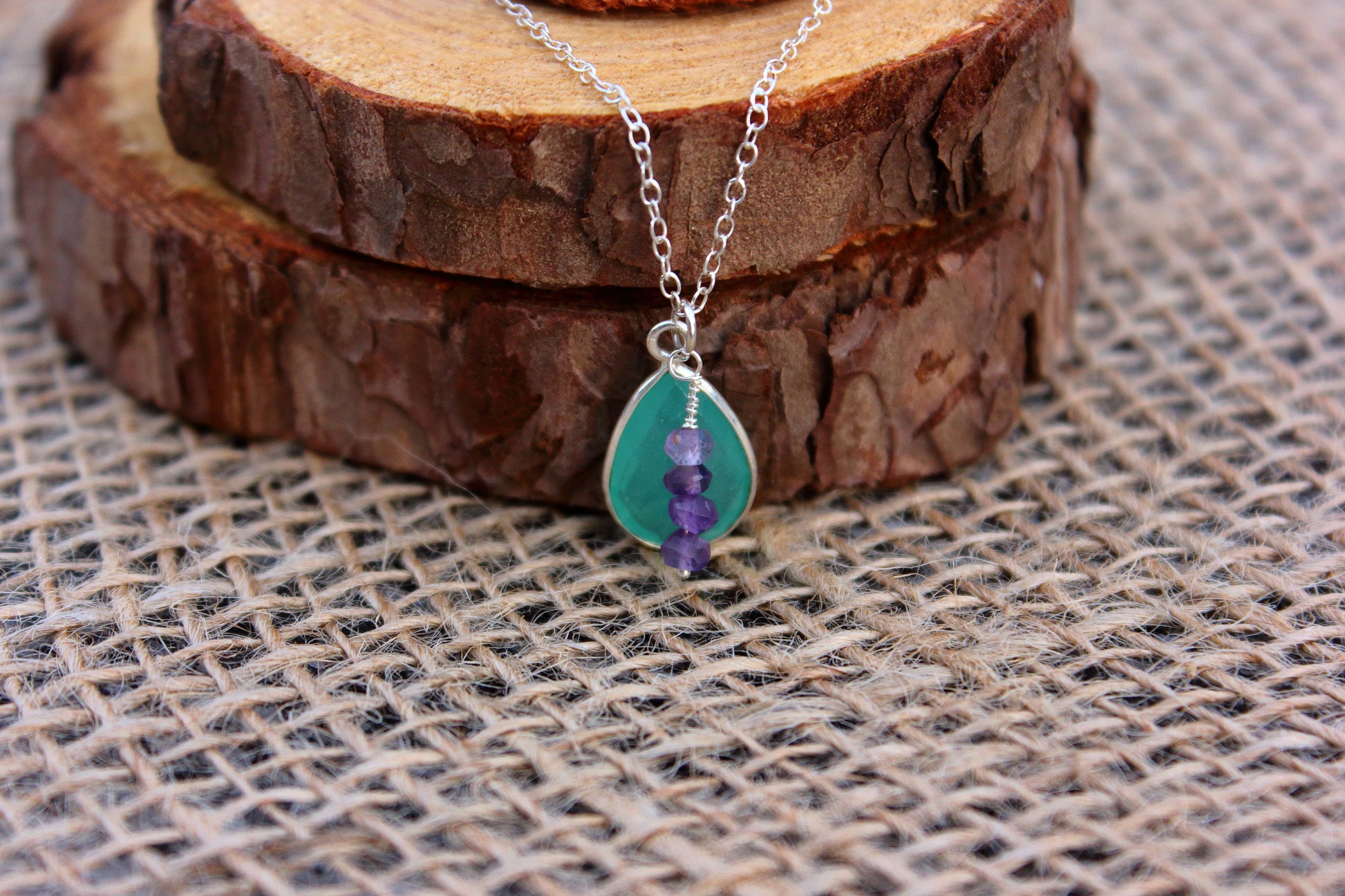Necklace with green pendant and purple bead on wooden surface