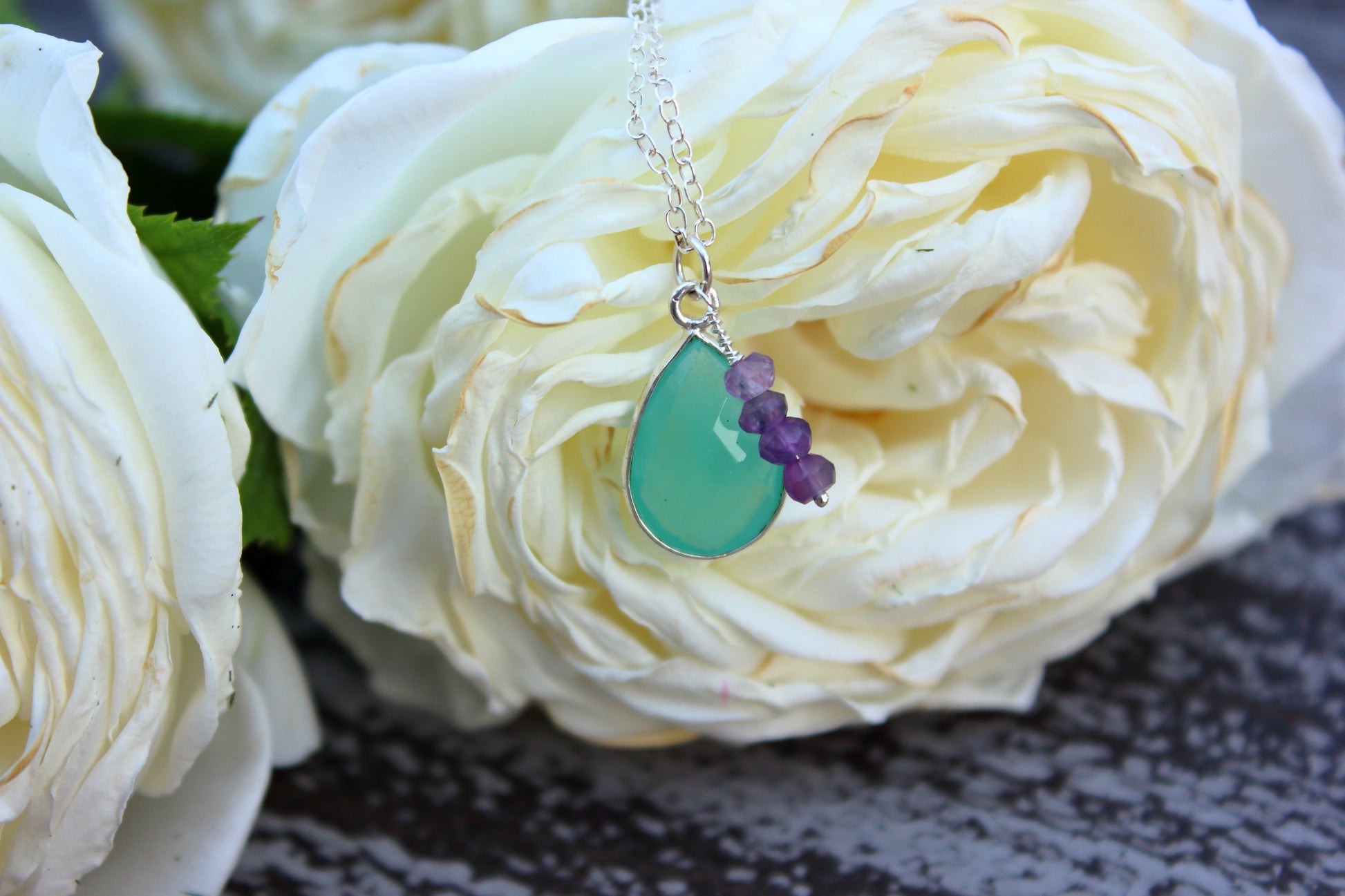 Necklace with a green teardrop pendant and purple beads on a white flower