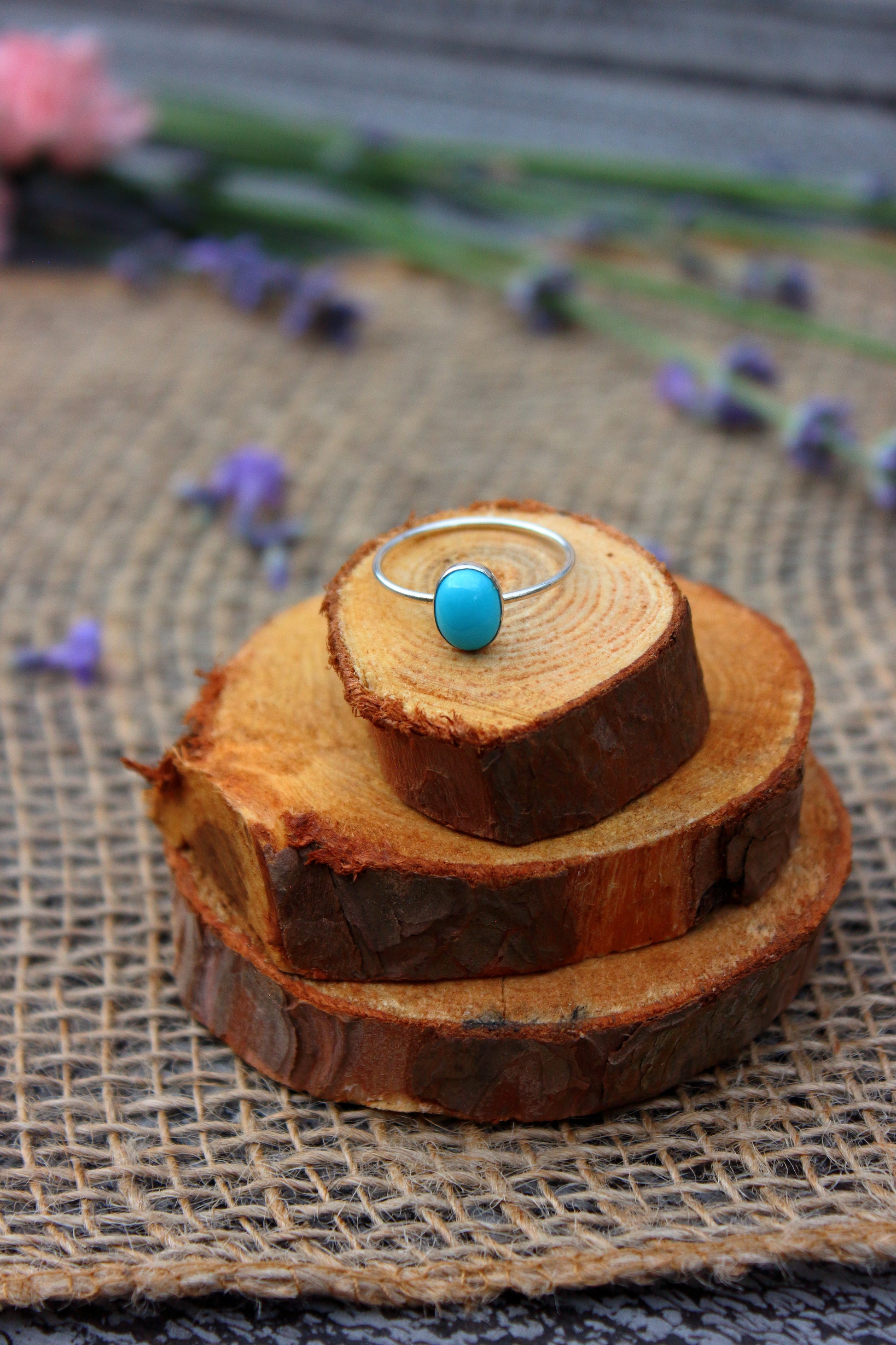 Silver ring with a blue gemstone on a stack of wooden slices with flowers in the background