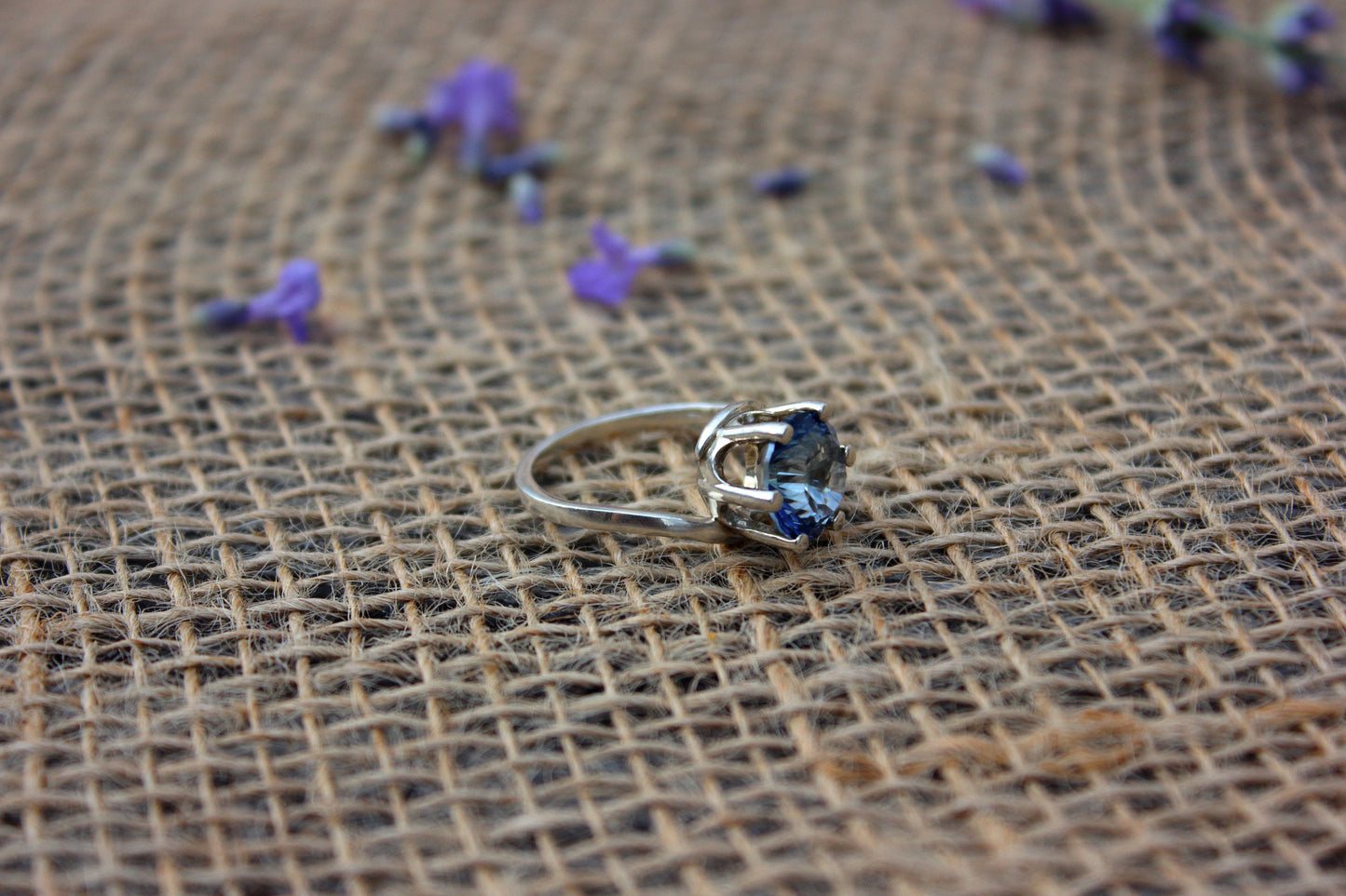 Silver ring with a blue gemstone on a textured brown surface with scattered purple flowers.