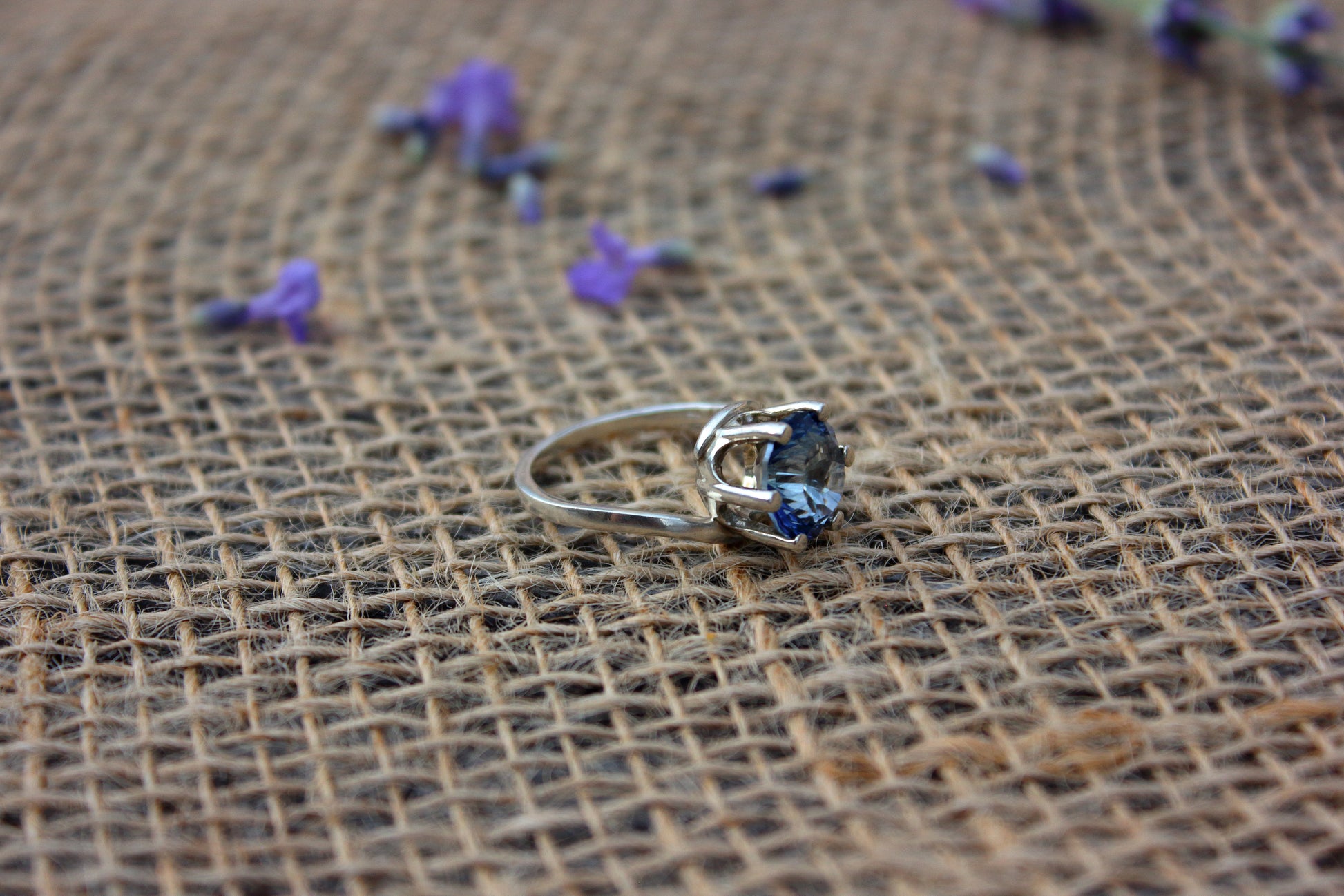 Silver ring with a blue gemstone on a textured brown surface with scattered purple flowers.