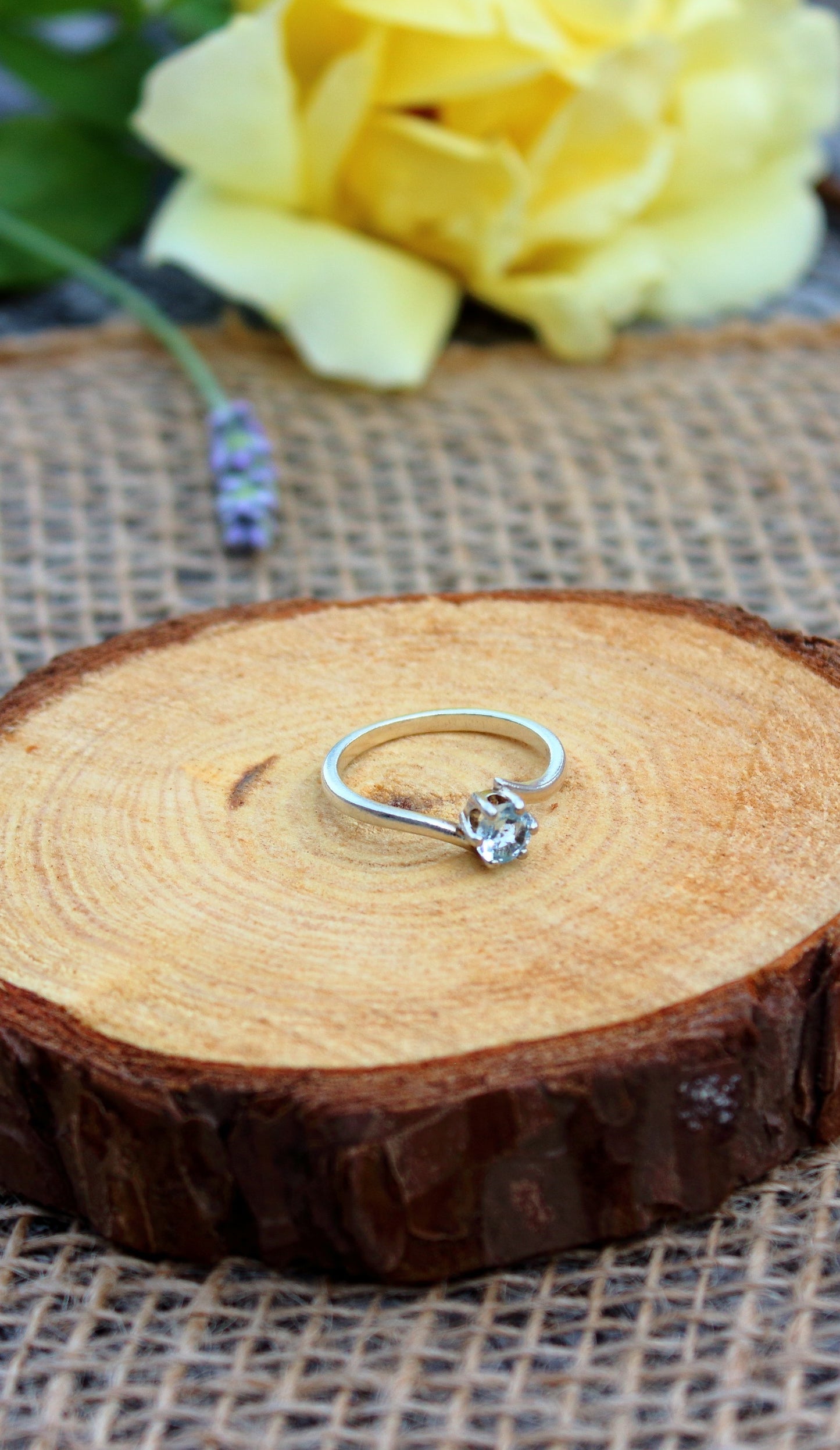Silver ring with a blue topaz on a wooden surface with yellow flowers in the background