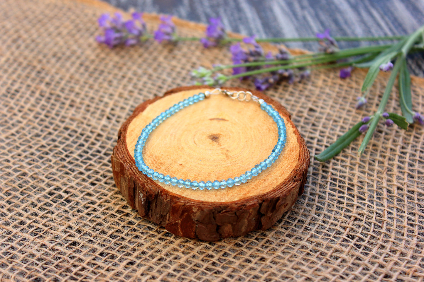 Blue beaded necklace on a wooden slice with lavender flowers on a rustic background
