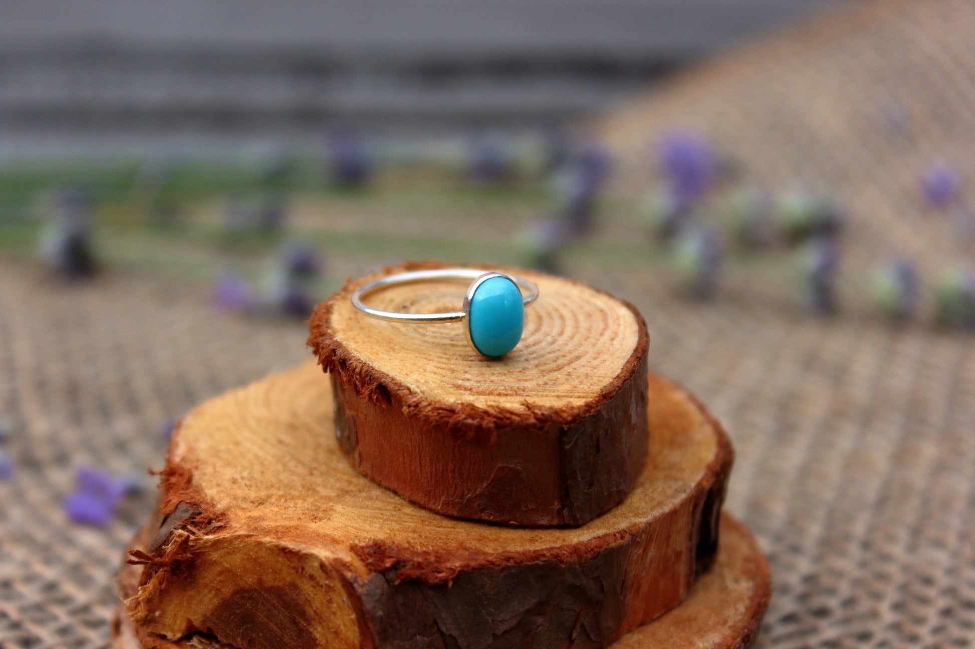 Silver ring with a turquoise stone on a wooden block with a blurred outdoor background