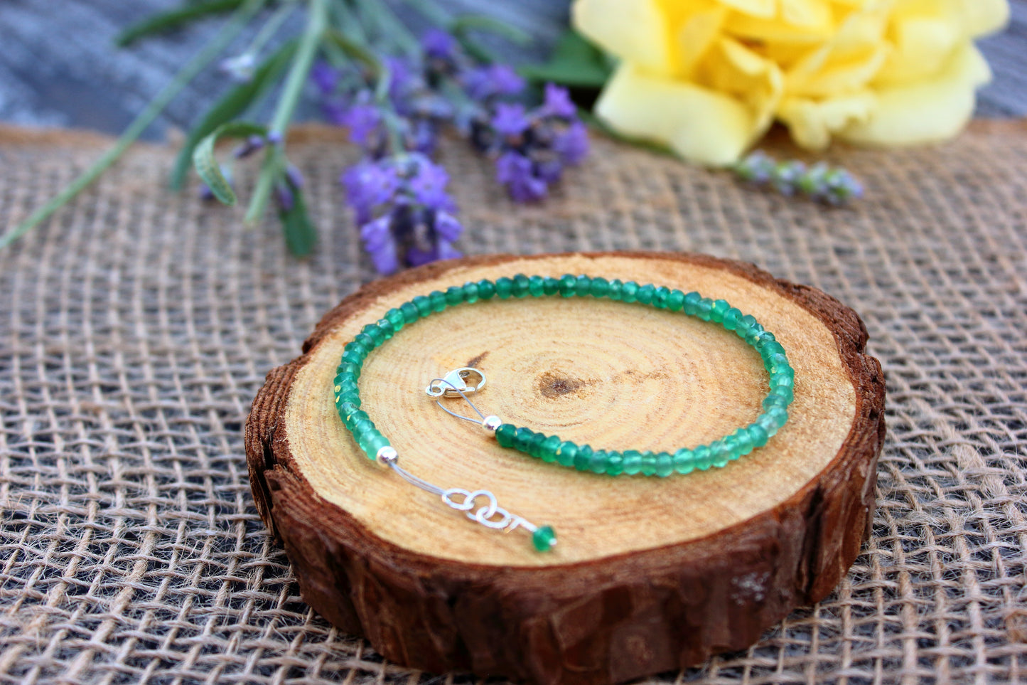 Green beaded bracelet on a wooden surface with flowers in the background