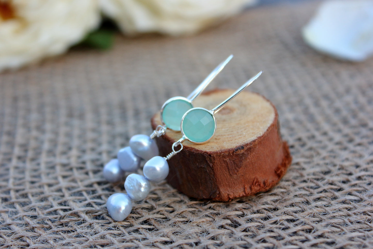 Pair of earrings with blue stones on a wooden block with a textured fabric background