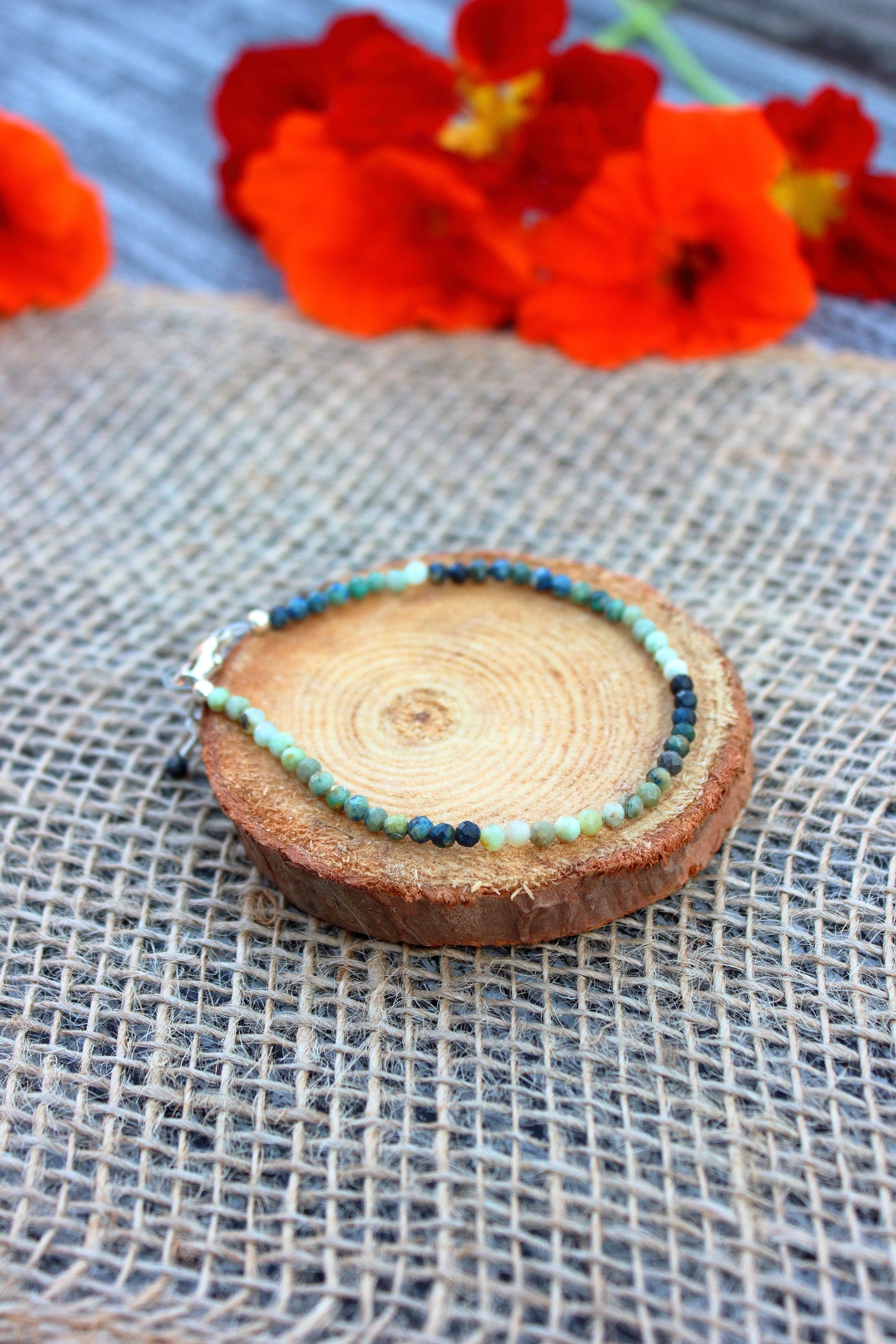Beaded bracelet on a wooden slice with red flowers in the background