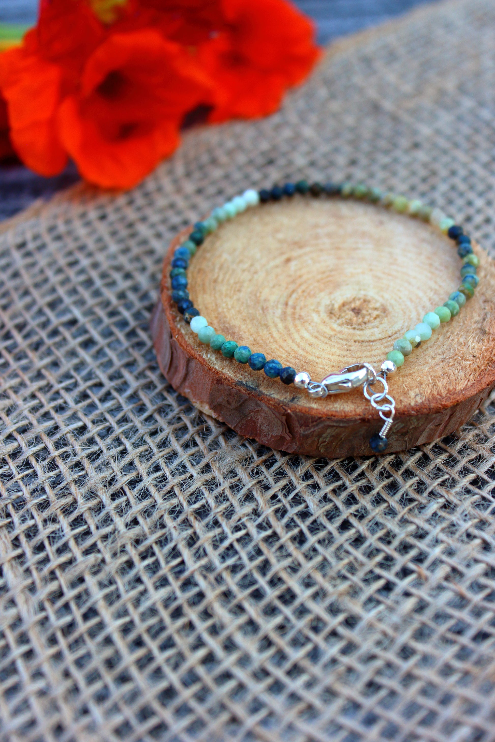 Beaded bracelet on a wooden slice with red flowers in the background