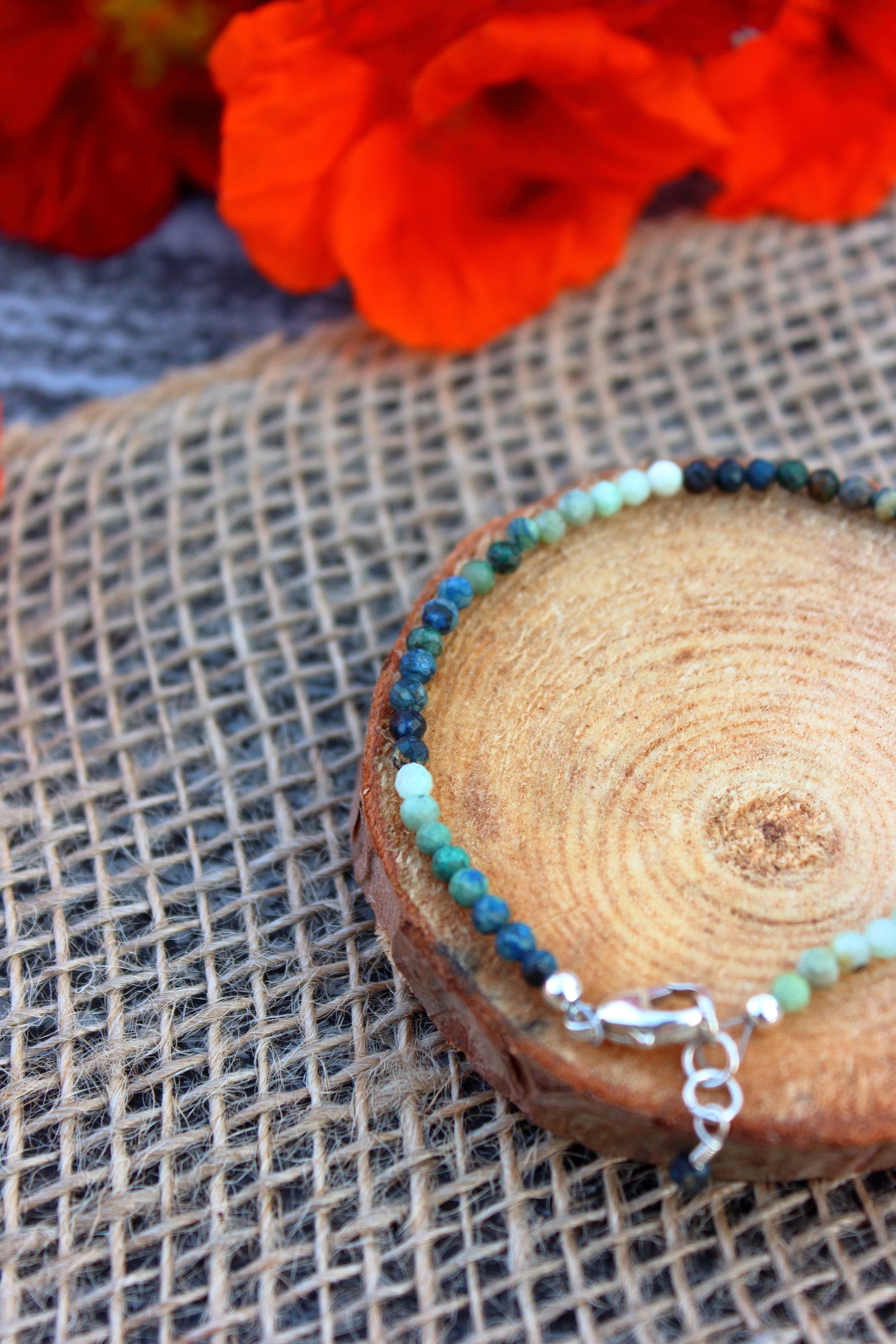 Bracelet with blue and green beads on a wooden surface with red flowers in the background