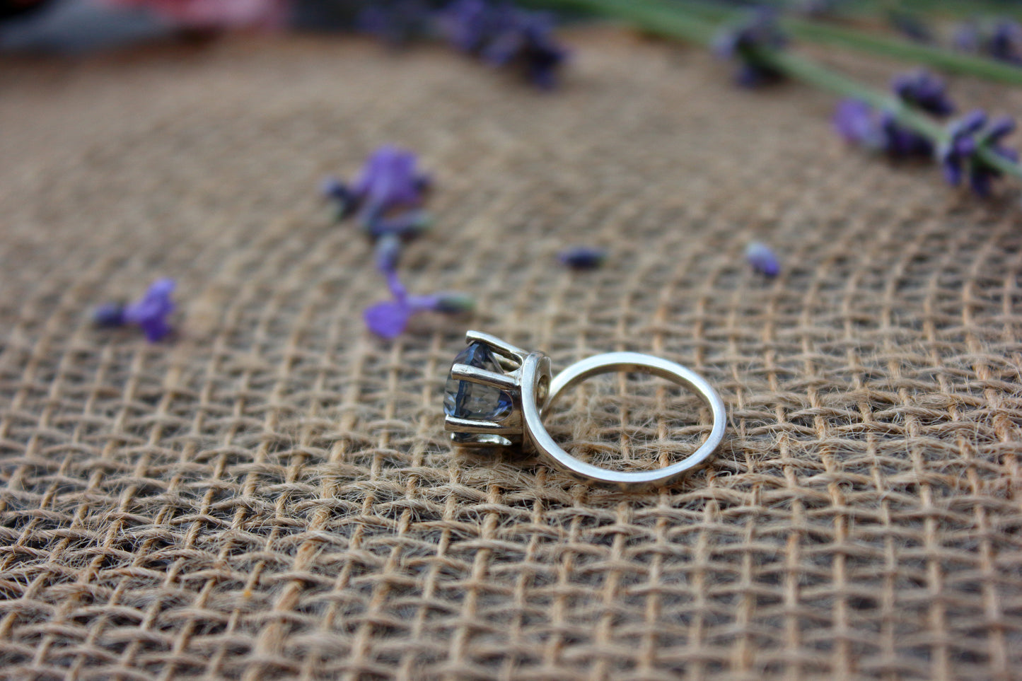 Silver ring with a gemstone on a textured brown surface with purple flowers.