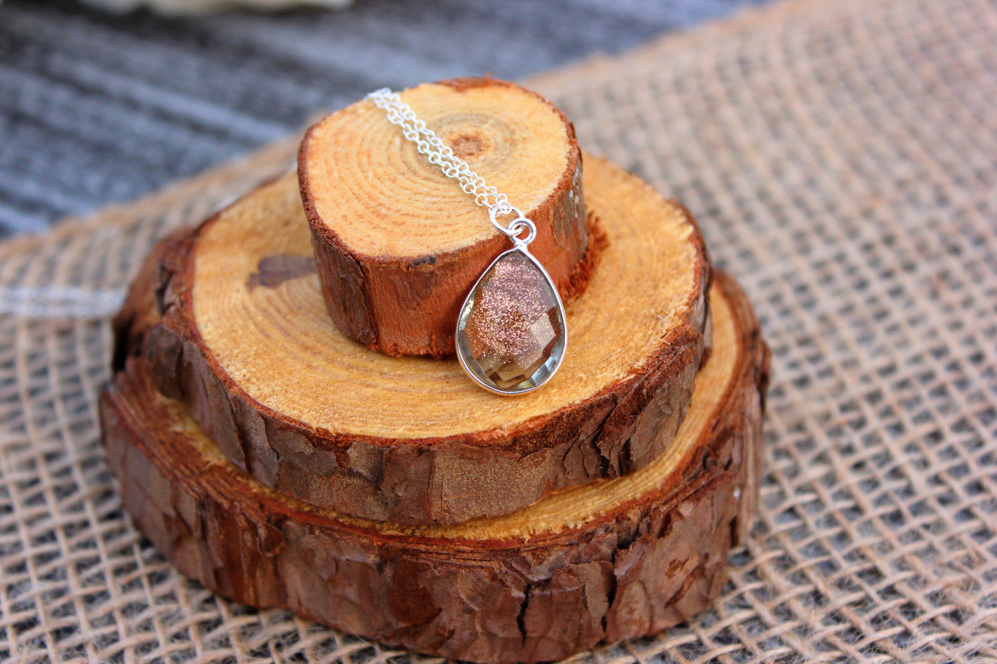 Silver teardrop pendant necklace on a wooden stand with a textured fabric background