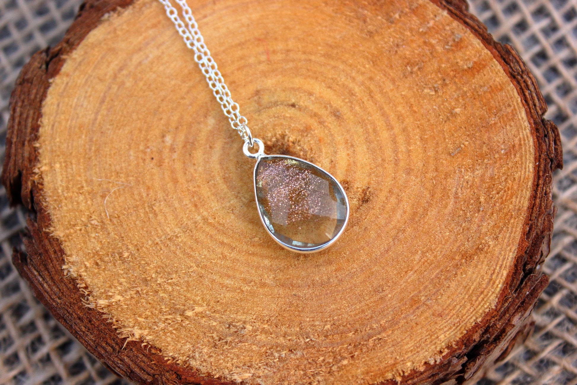 Teardrop-shaped pendant on a chain on a wooden surface