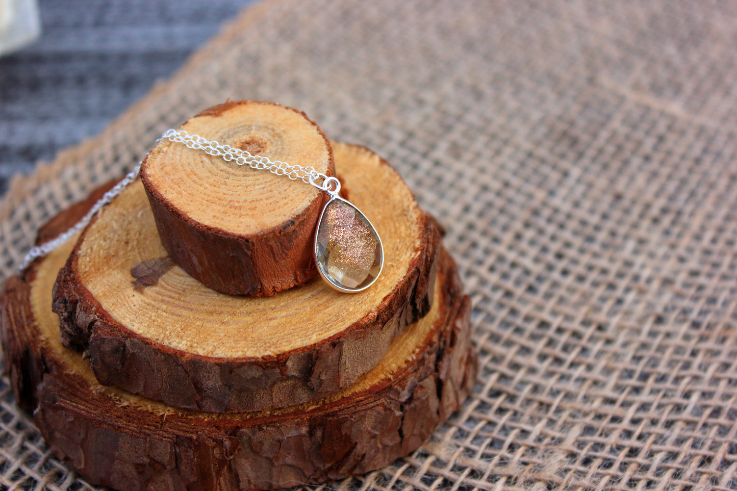 Teardrop-shaped pendant on a chain displayed on wooden slices with a textured fabric background