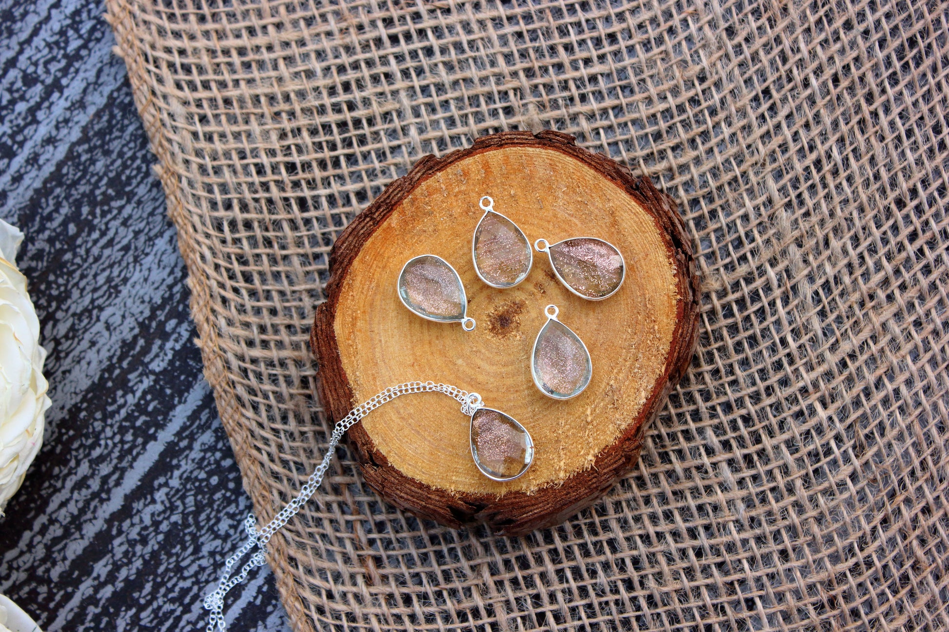 Silver teardrop-shaped jewelry set on a wooden block with a textured fabric background