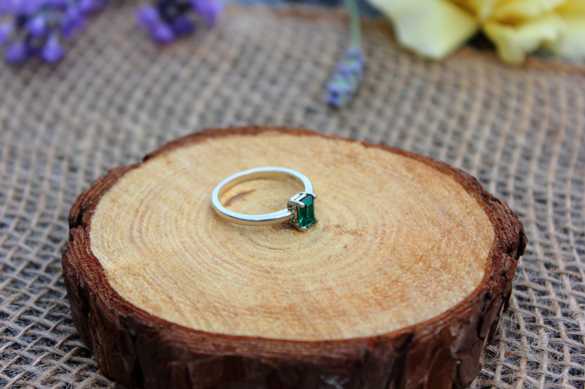 Silver ring with a green gemstone on a wooden surface with flowers in the background