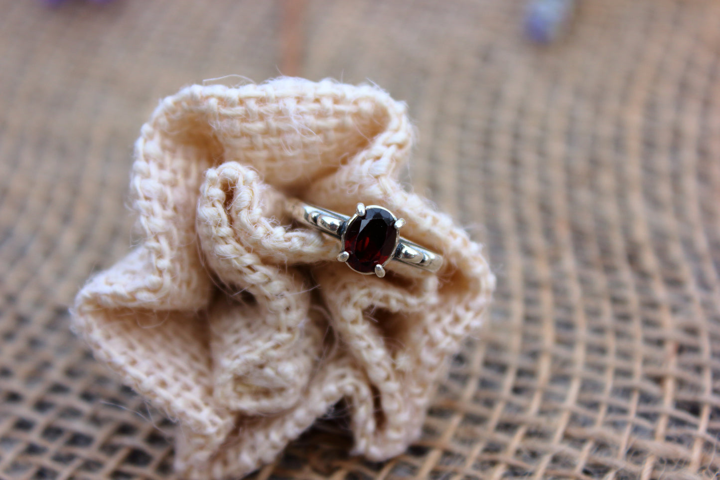 Silver ring with a dark gemstone on a knitted beige flower