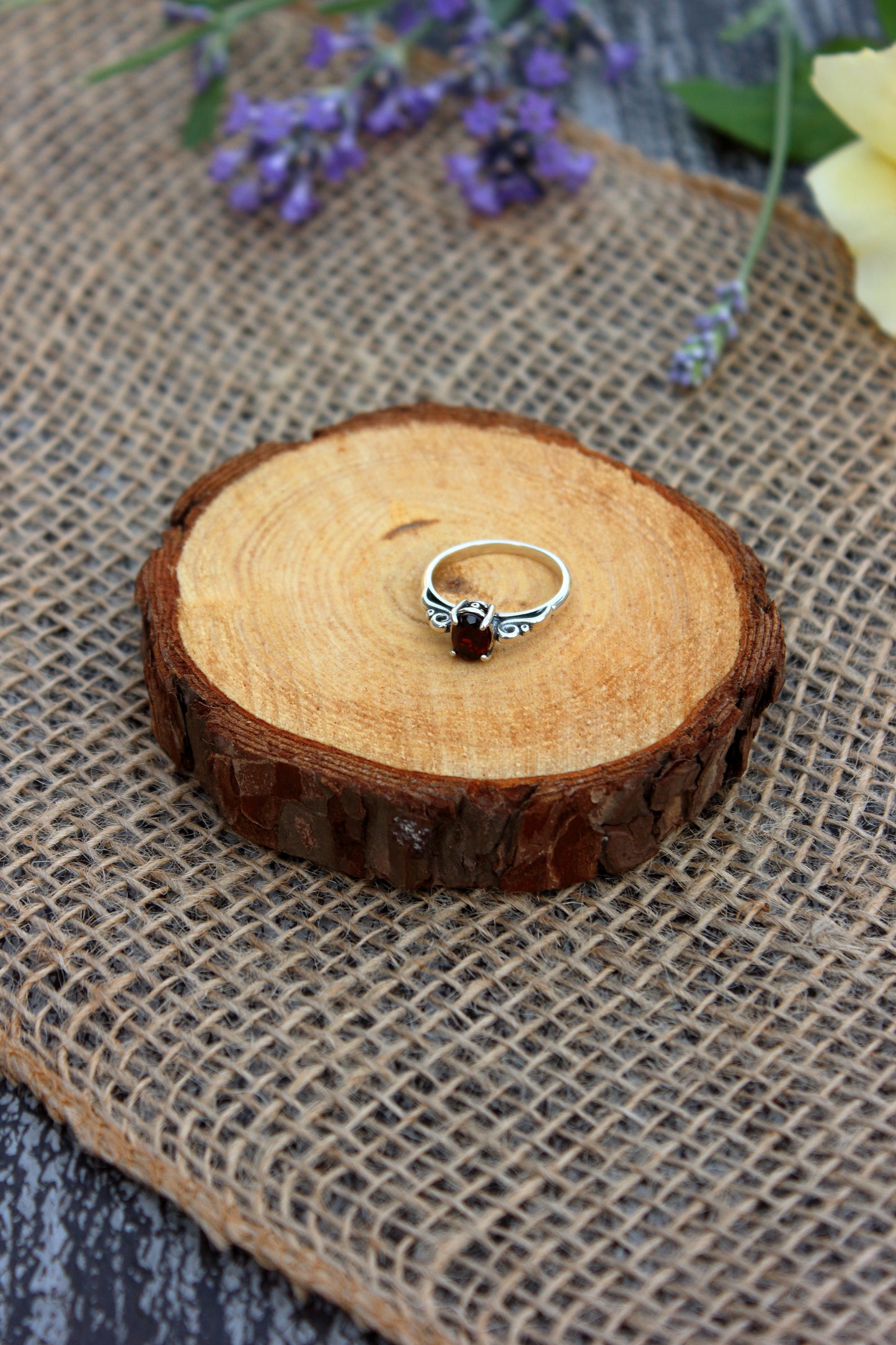 Silver ring on a wooden slice with flowers in the background