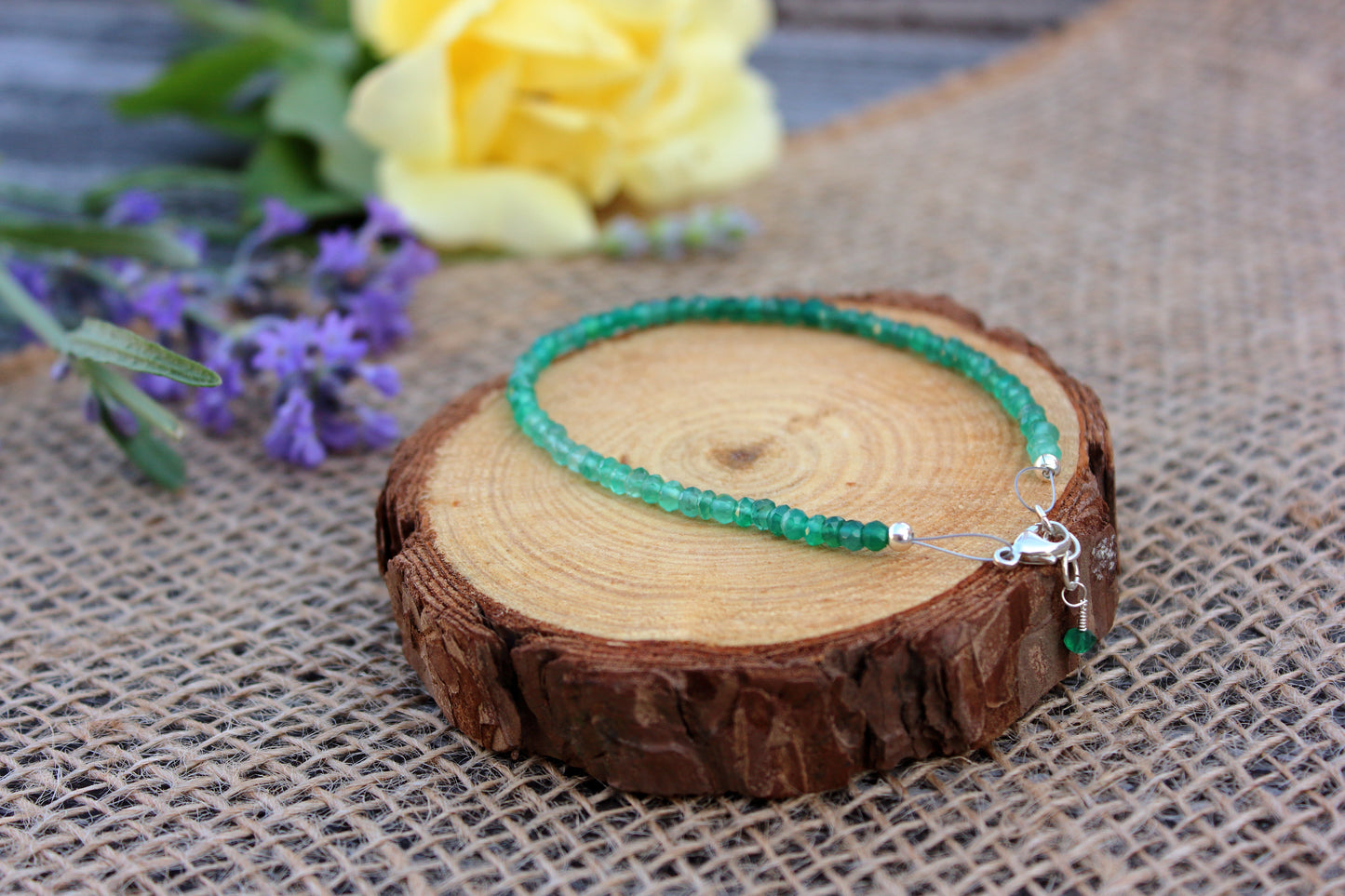 Green beaded bracelet on a wooden slice with flowers in the background