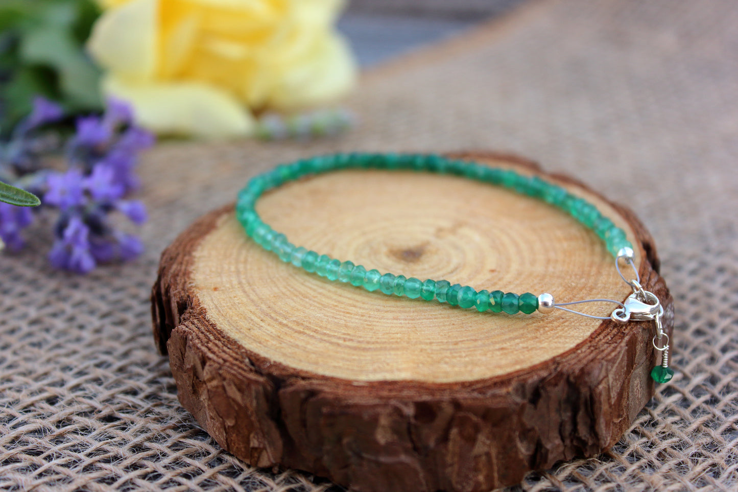 Green beaded necklace on a wooden surface with flowers in the background