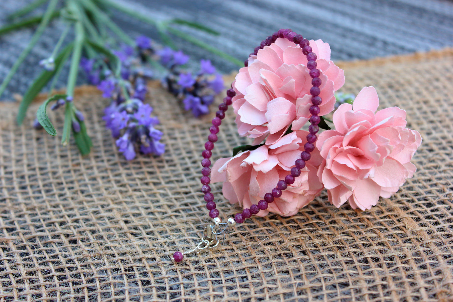 Pink flowers and a ruby bracelet on a textured surface with lavender in the background.
