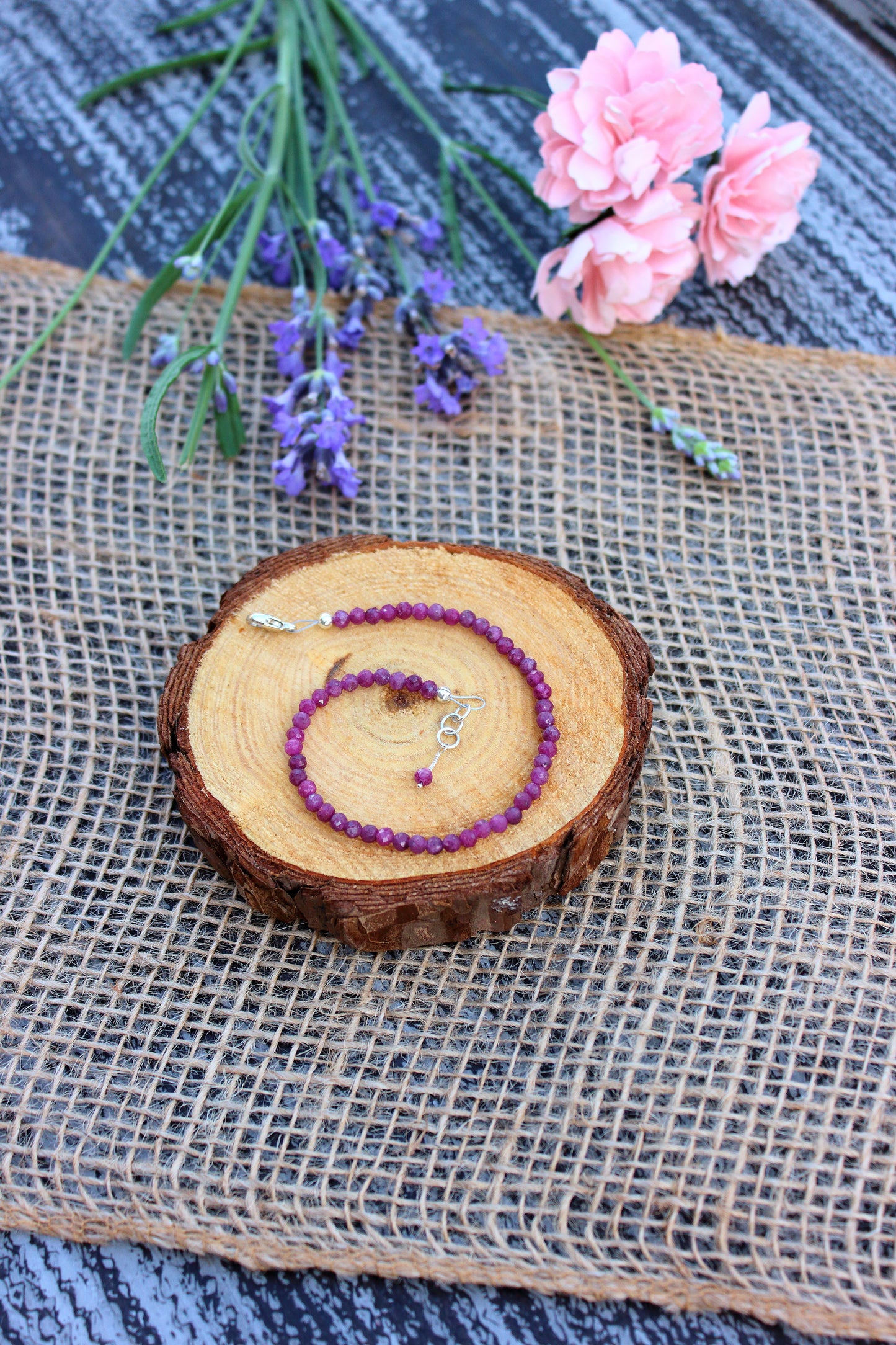 Ruby beaded bracelet on a wooden slice with flowers and burlap in the background