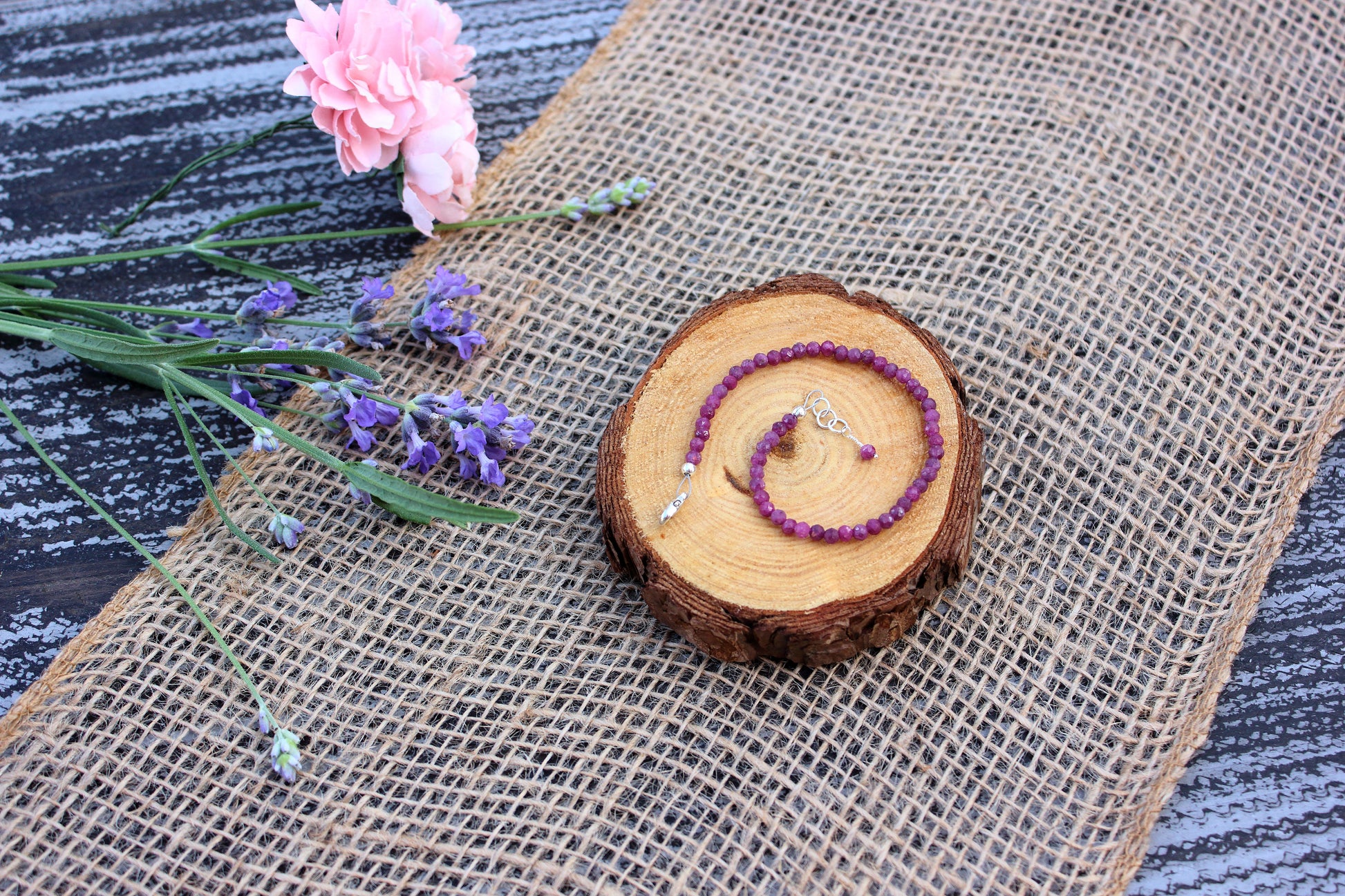 Ruby beaded necklace on a wooden slice with flowers and burlap in the background