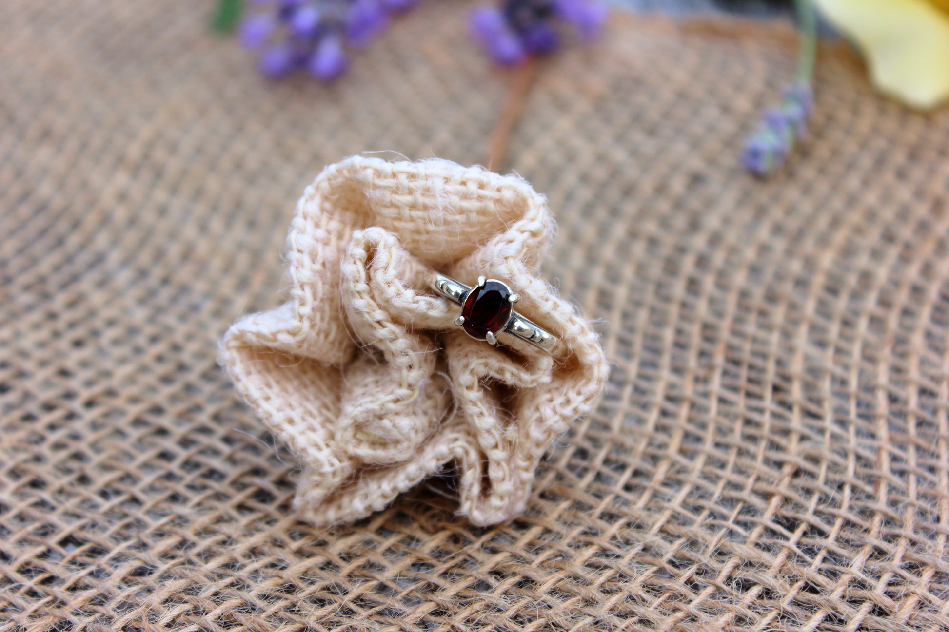 Ring with a dark stone on a beige fabric flower against a rustic background