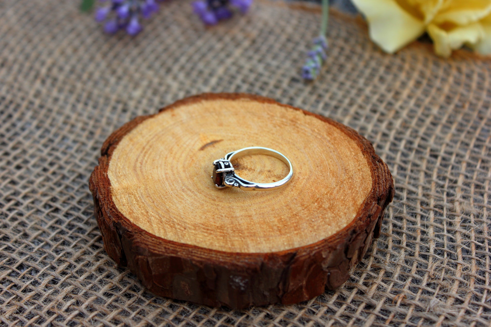 Silver ring on a wooden slice with flowers in the background