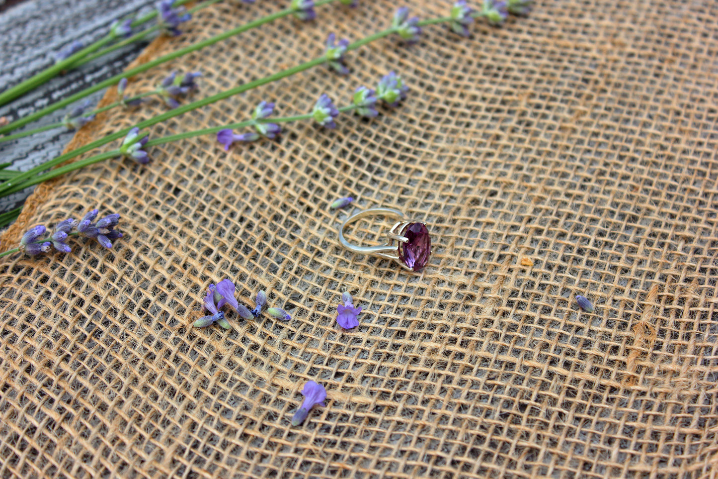 Ring with a purple gemstone on a textured fabric background with lavender flowers.