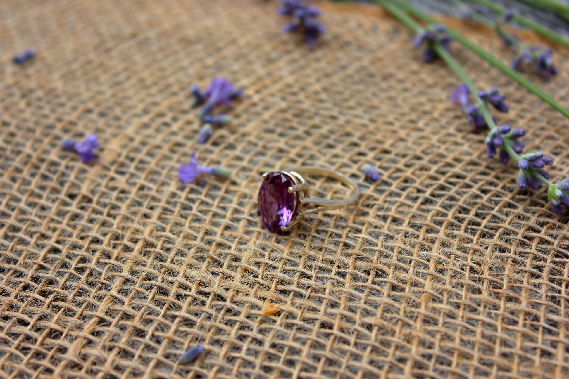 Ring with a purple gemstone on a textured brown surface with scattered lavender flowers.