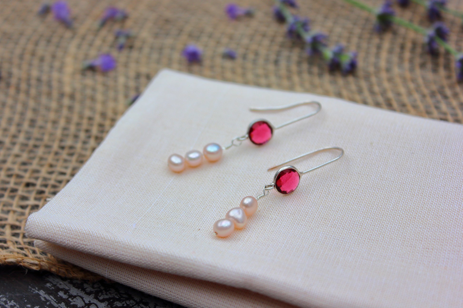 Pair of earrings with red and pearl-like stones on a beige fabric background