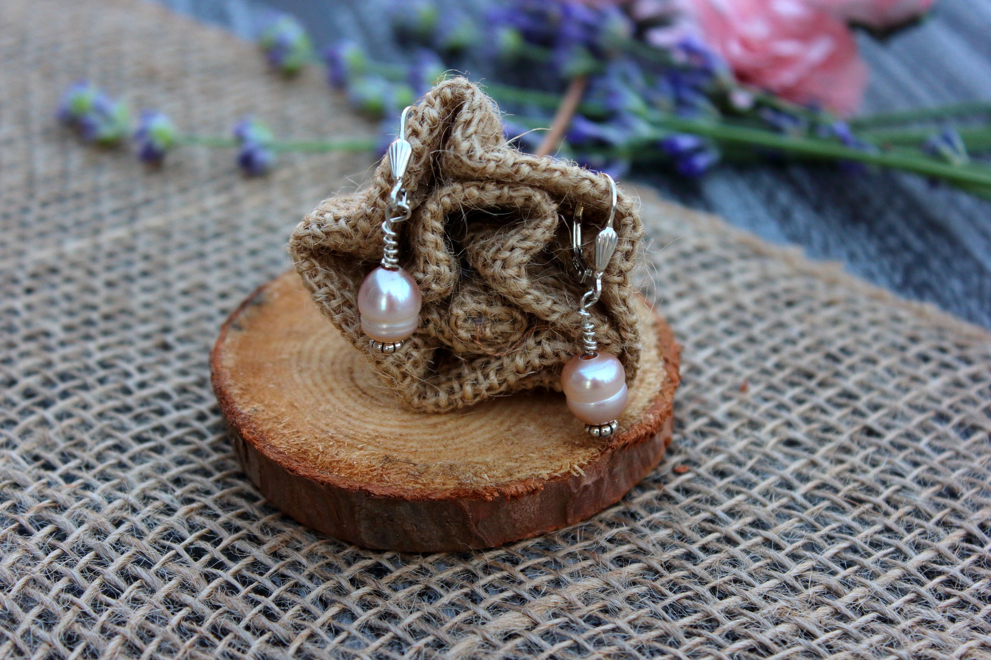 Pair of pearl earrings on a wooden stand with burlap and floral background