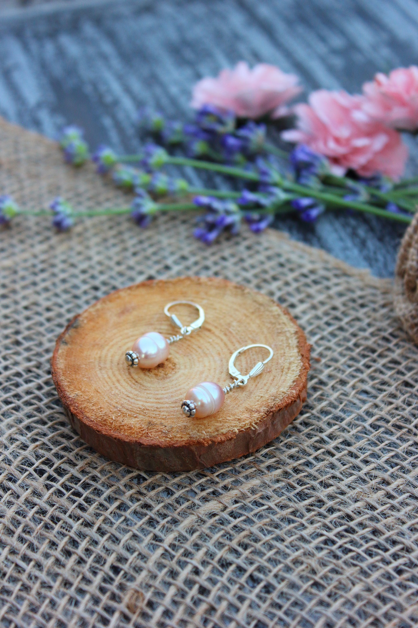 Pair of pearl earrings on a wooden slice with flowers in the background