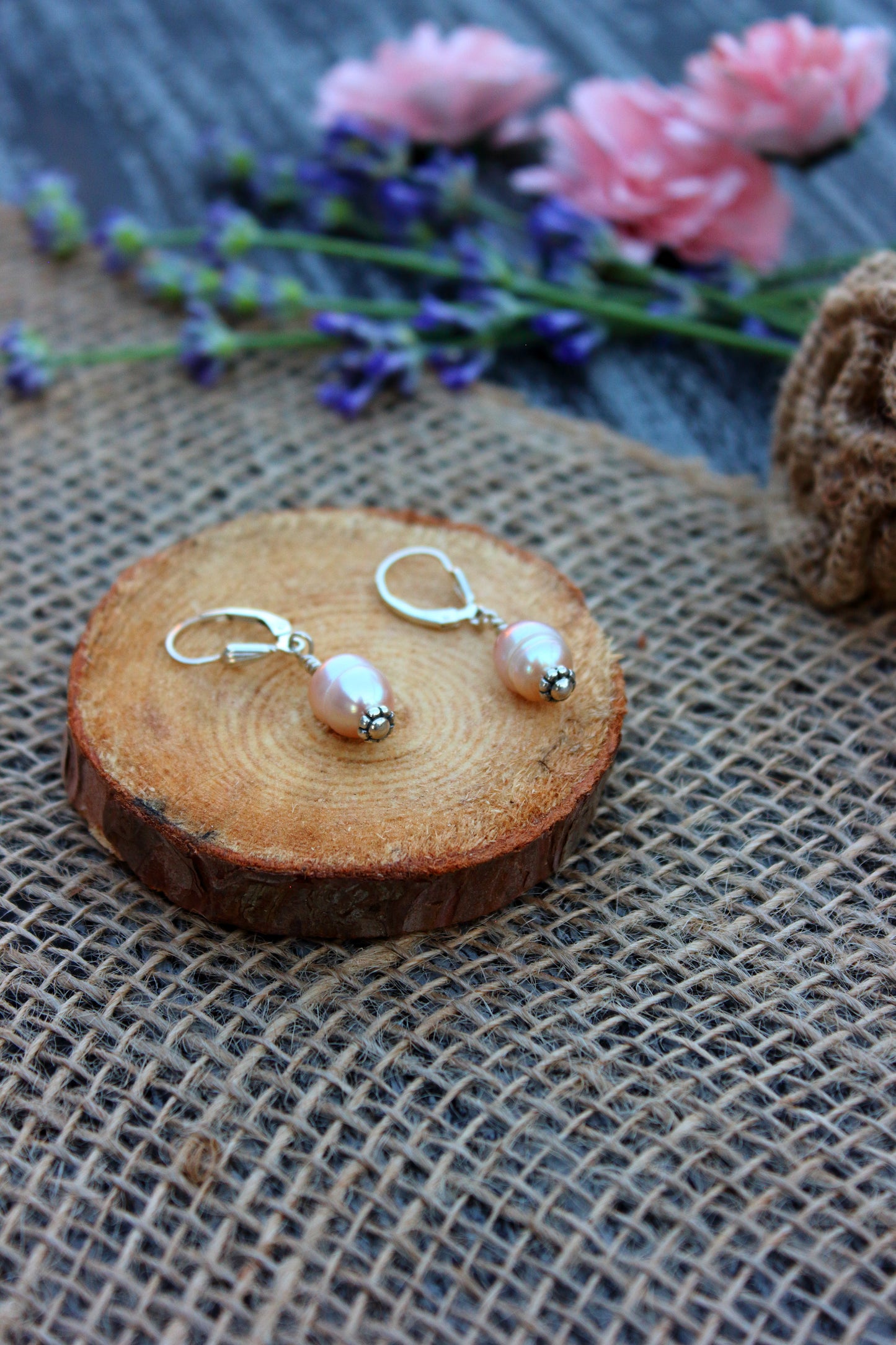 Pair of pearl earrings on a wooden slice with flowers in the background