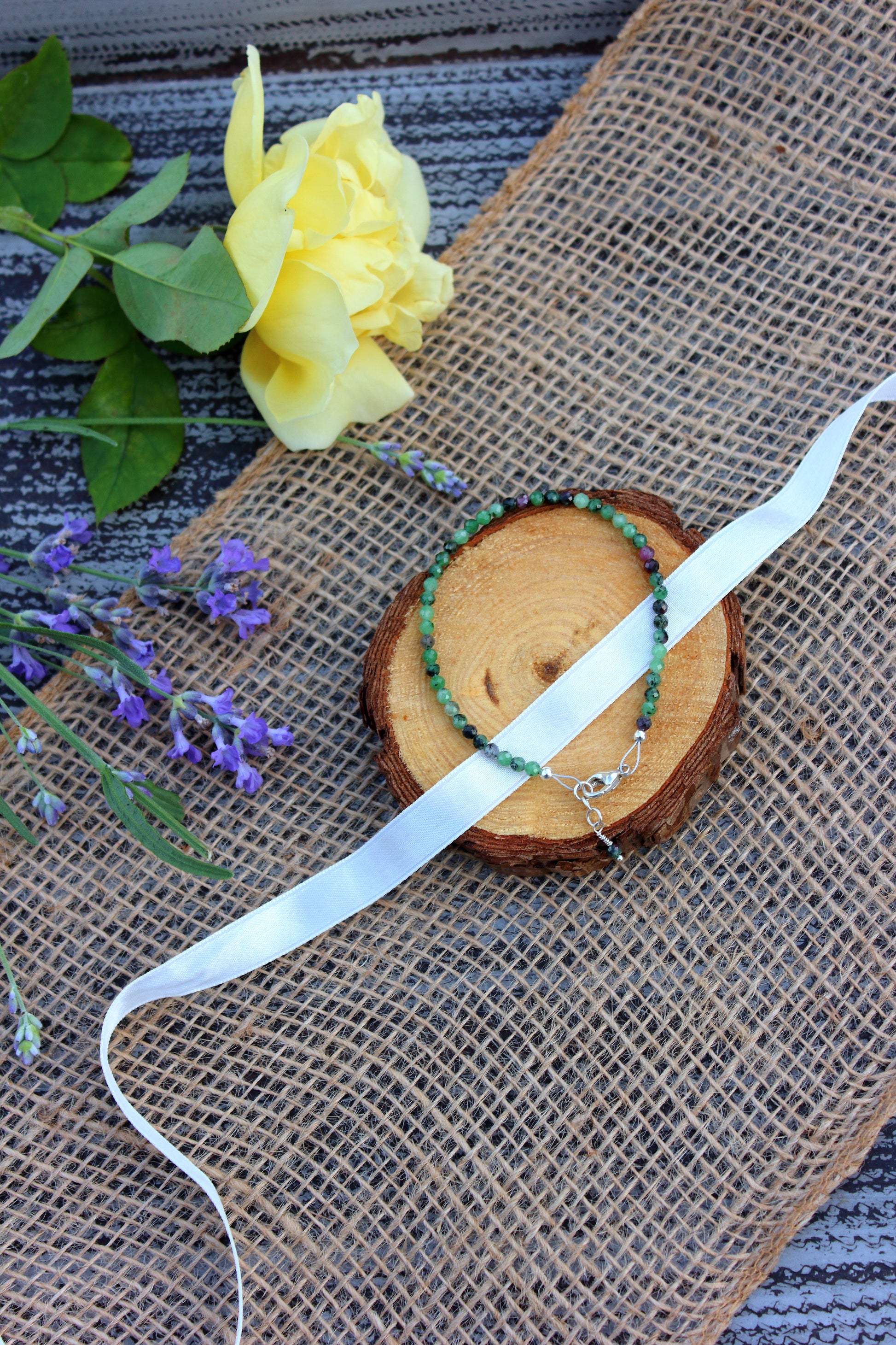 Bracelet on a wooden slice with a yellow rose and lavender flowers on a textured surface