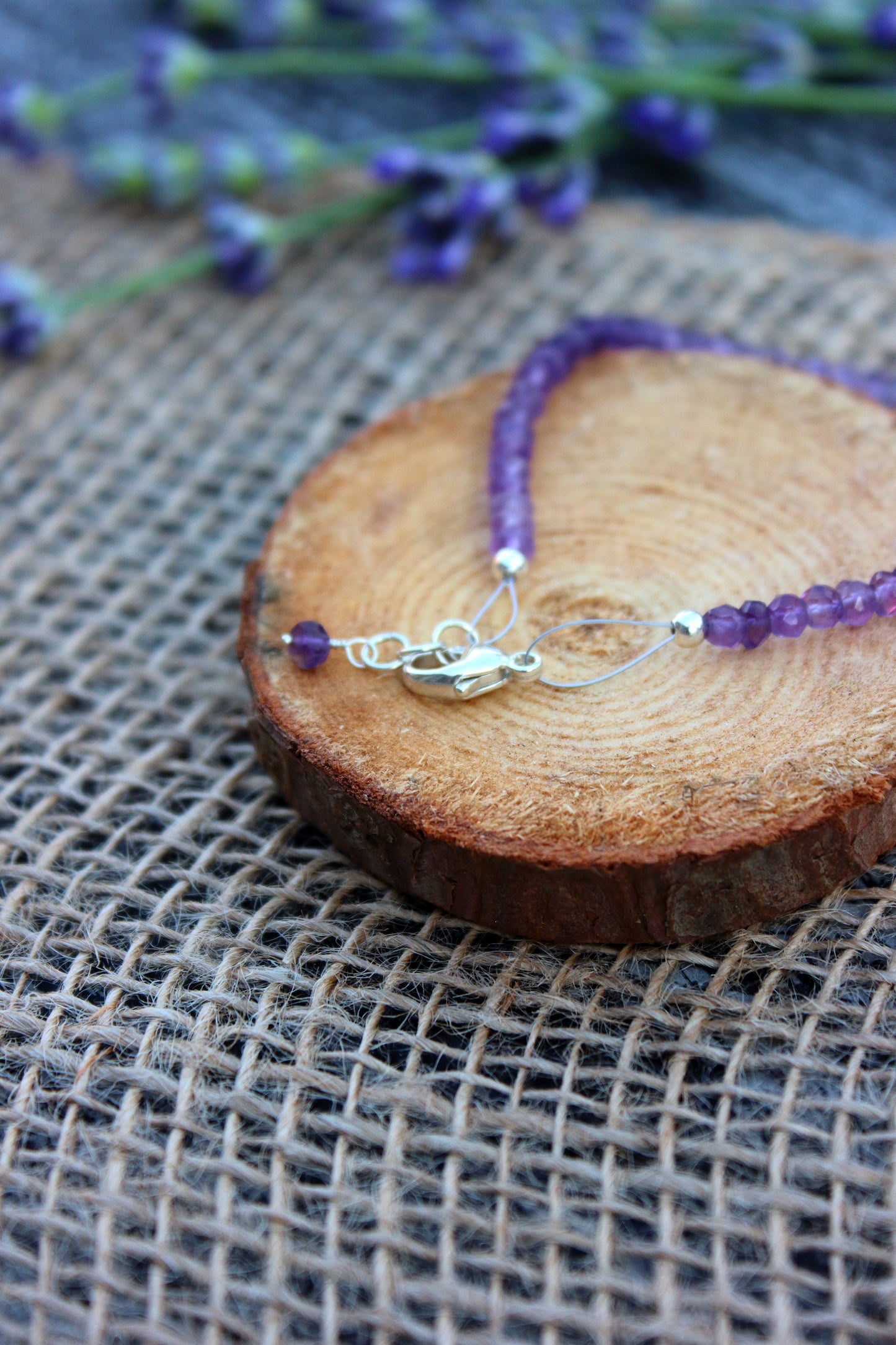Amethyst beaded bracelet with a silver charm on a wooden slice with lavender in the background