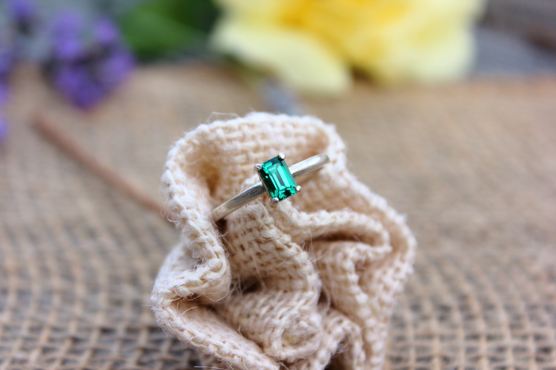 Ring with a green gemstone on a knitted fabric with flowers in the background