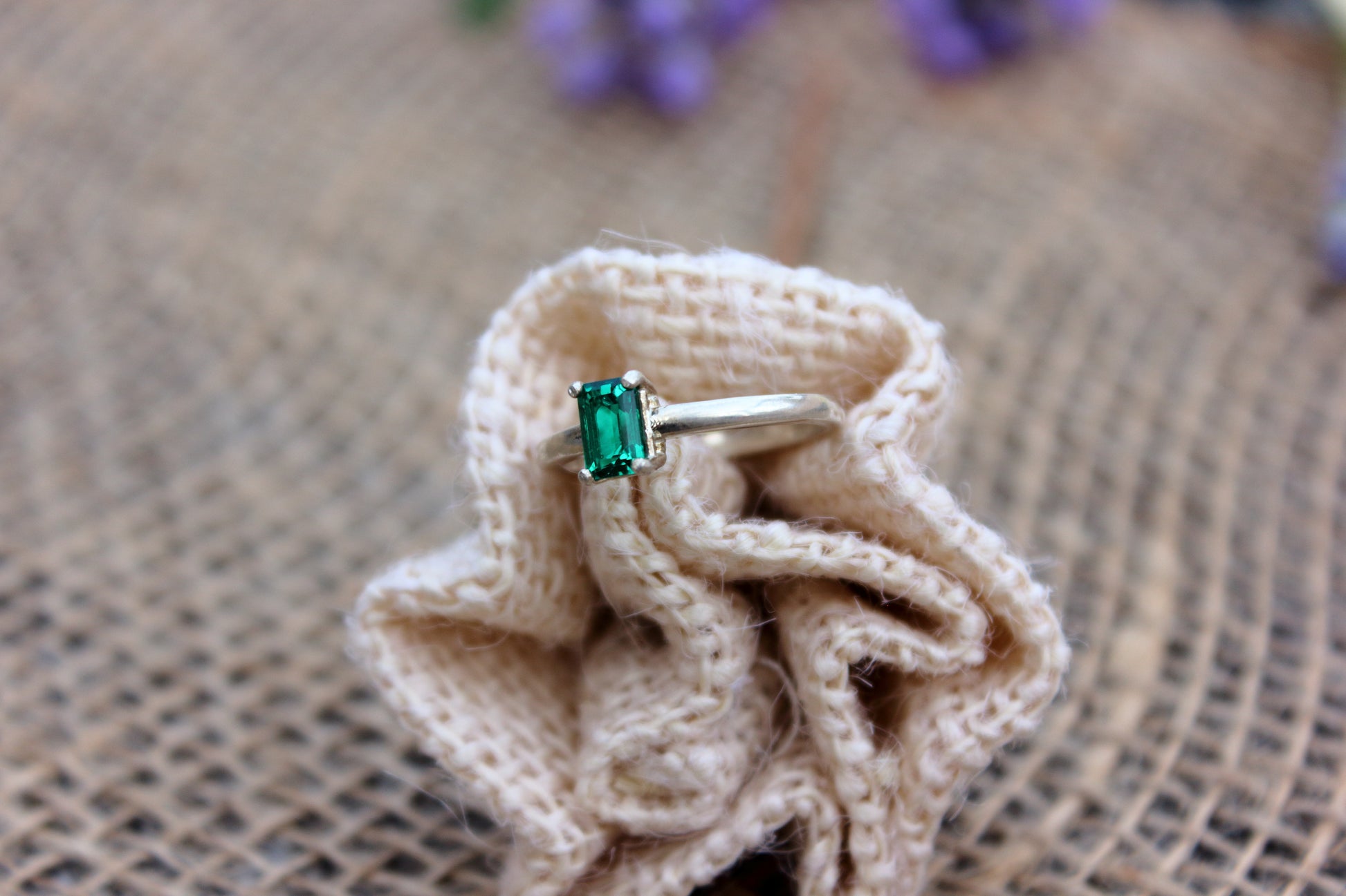 Ring with a green gemstone on a knitted fabric with a burlap background