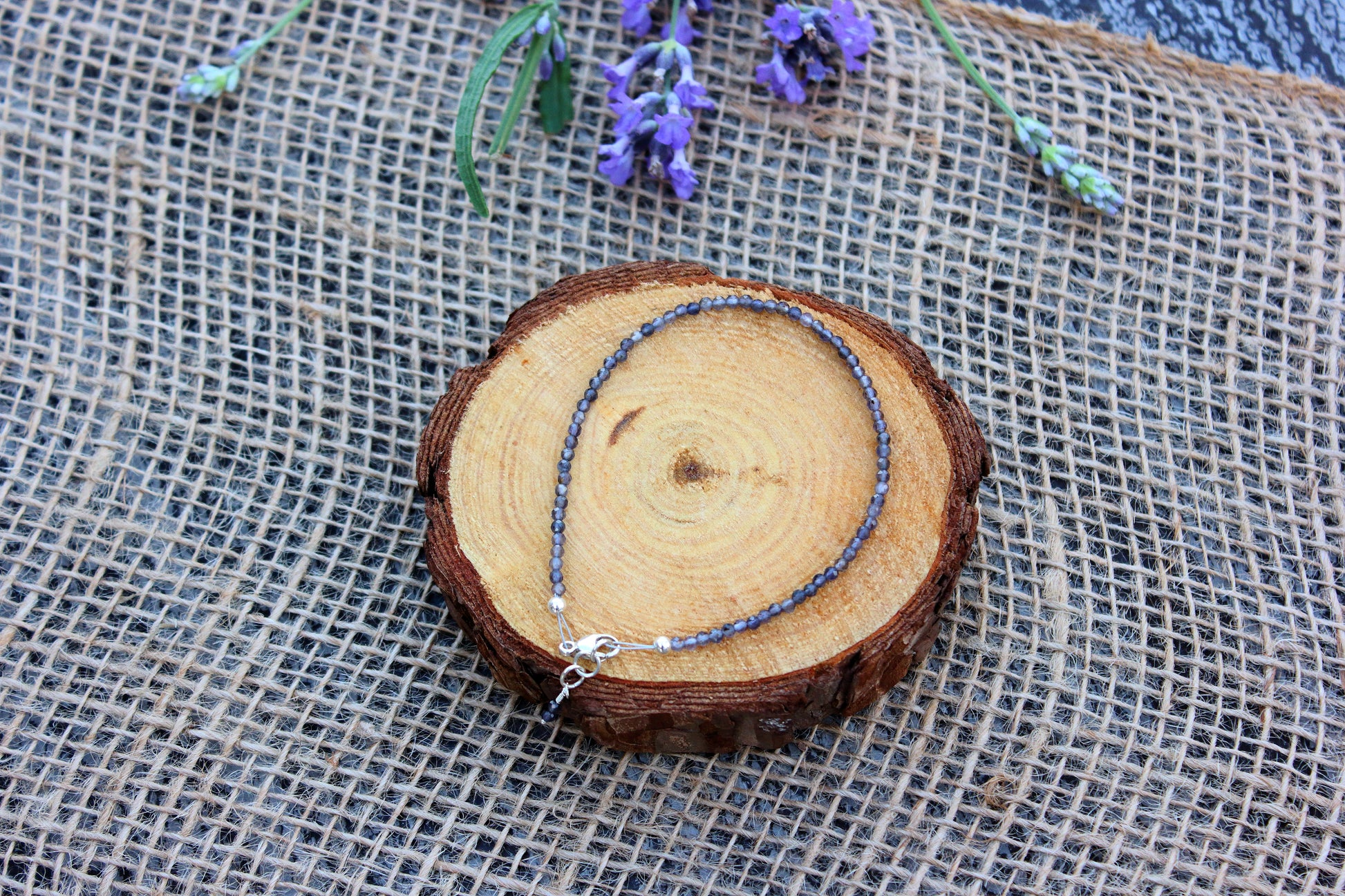 Bracelet on a wooden slice with lavender flowers on a textured fabric background