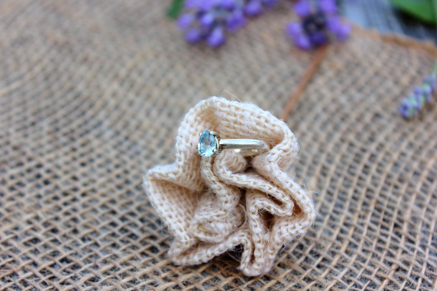 Ring with a blue gemstone on a knitted fabric piece against a textured background