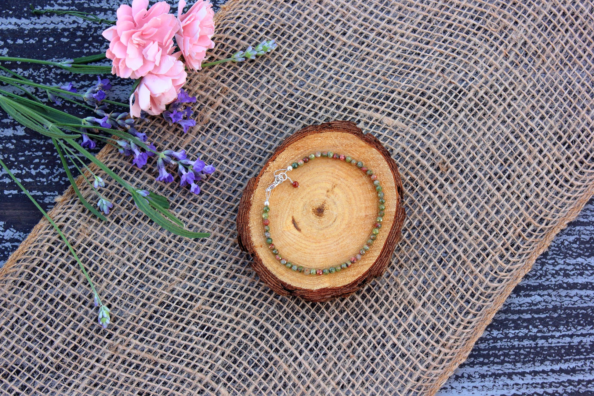Bracelet on a wooden coaster with pink flowers and lavender on a textured surface